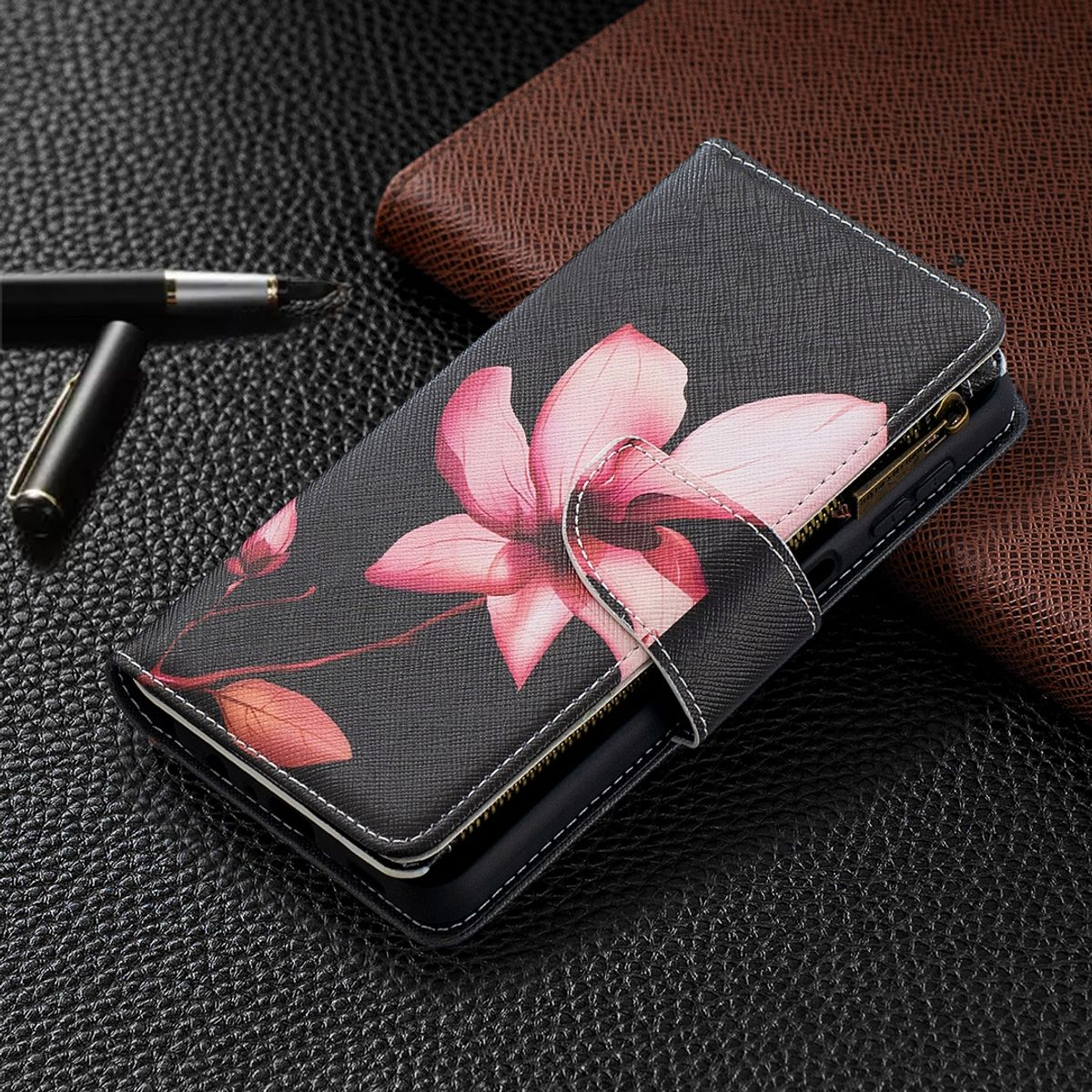Schwarze Handyhülle mit pinkfarbenem Blumendesign, weißen Nähten und braunem Hintergrund.