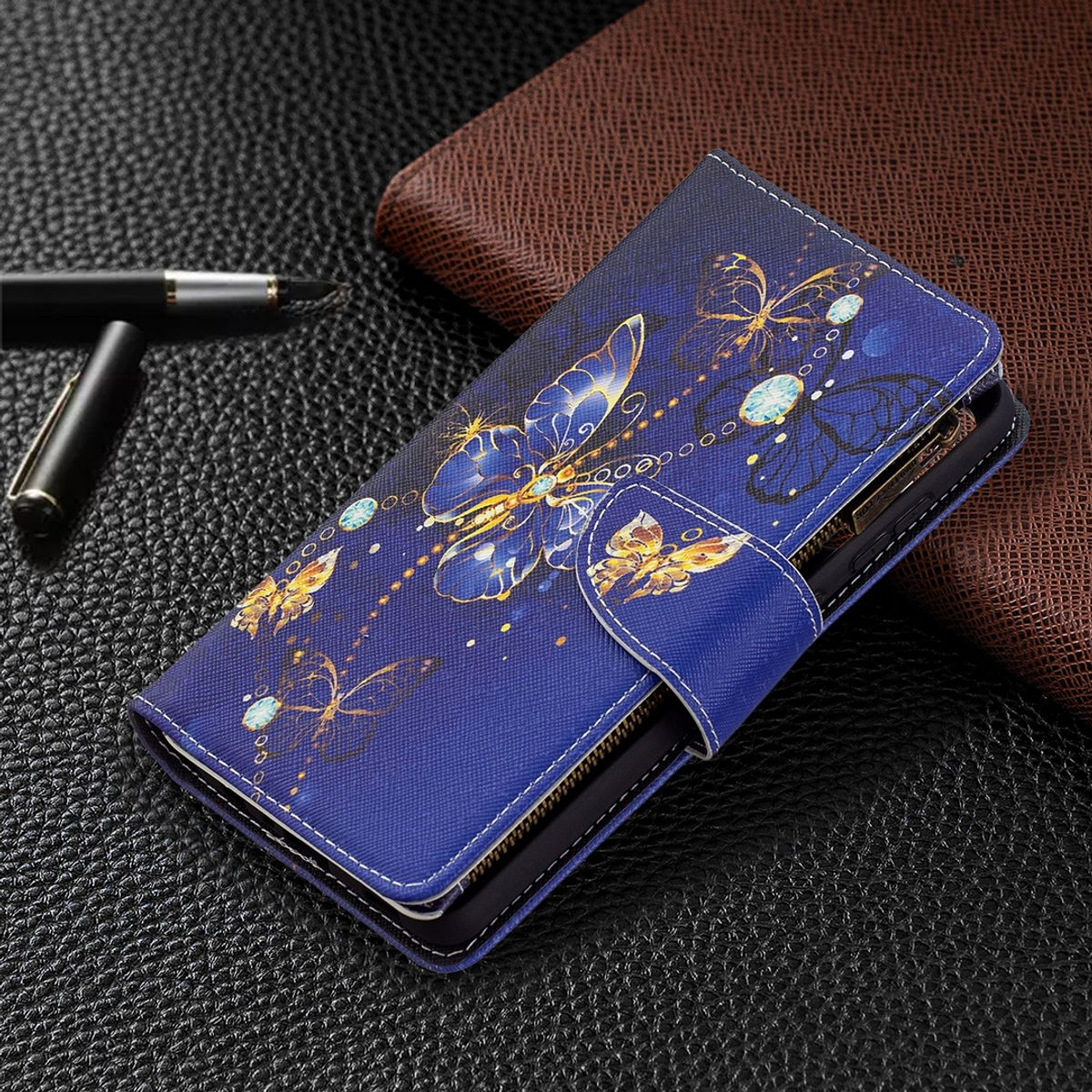 Blaue Handyhülle mit Schmetterlingsdesign. Weiße Nähte. Auf dunkler Oberfläche mit braunem Portemonnaie.