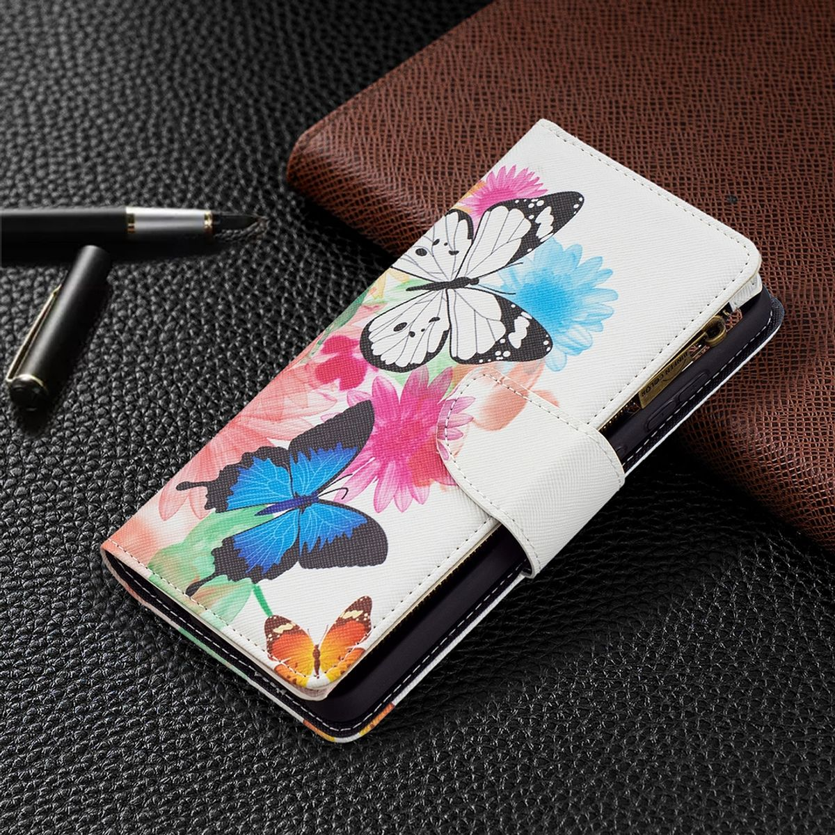 Weisse Handyhülle mit Schmetterlingen und Blumen auf schwarzem Untergrund mit Stift.