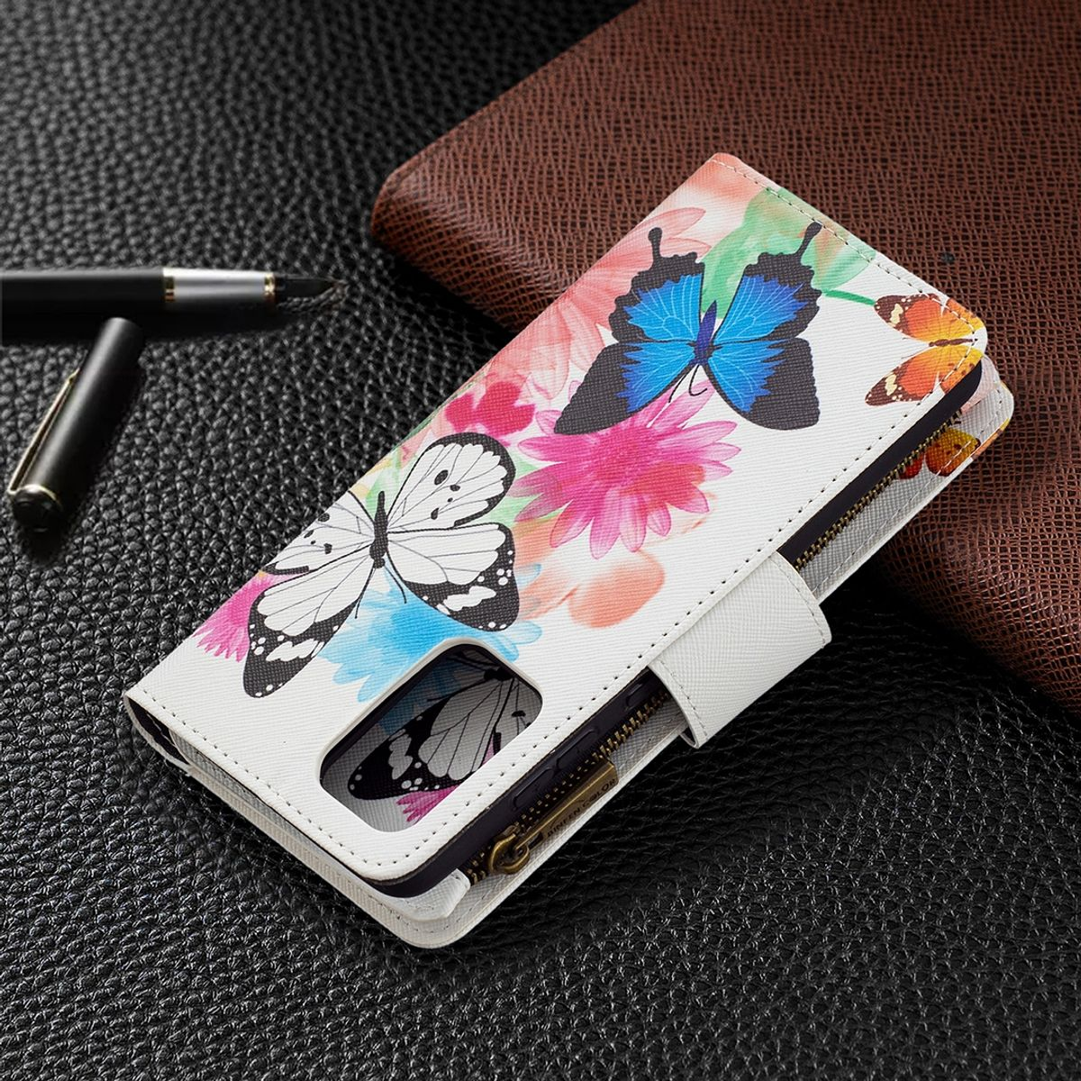 Eine weiße Handyhülle mit floralem Design. Schmetterlinge und Blumen sind darauf. Ein Stift und eine Brieftasche sind im Hintergrund.