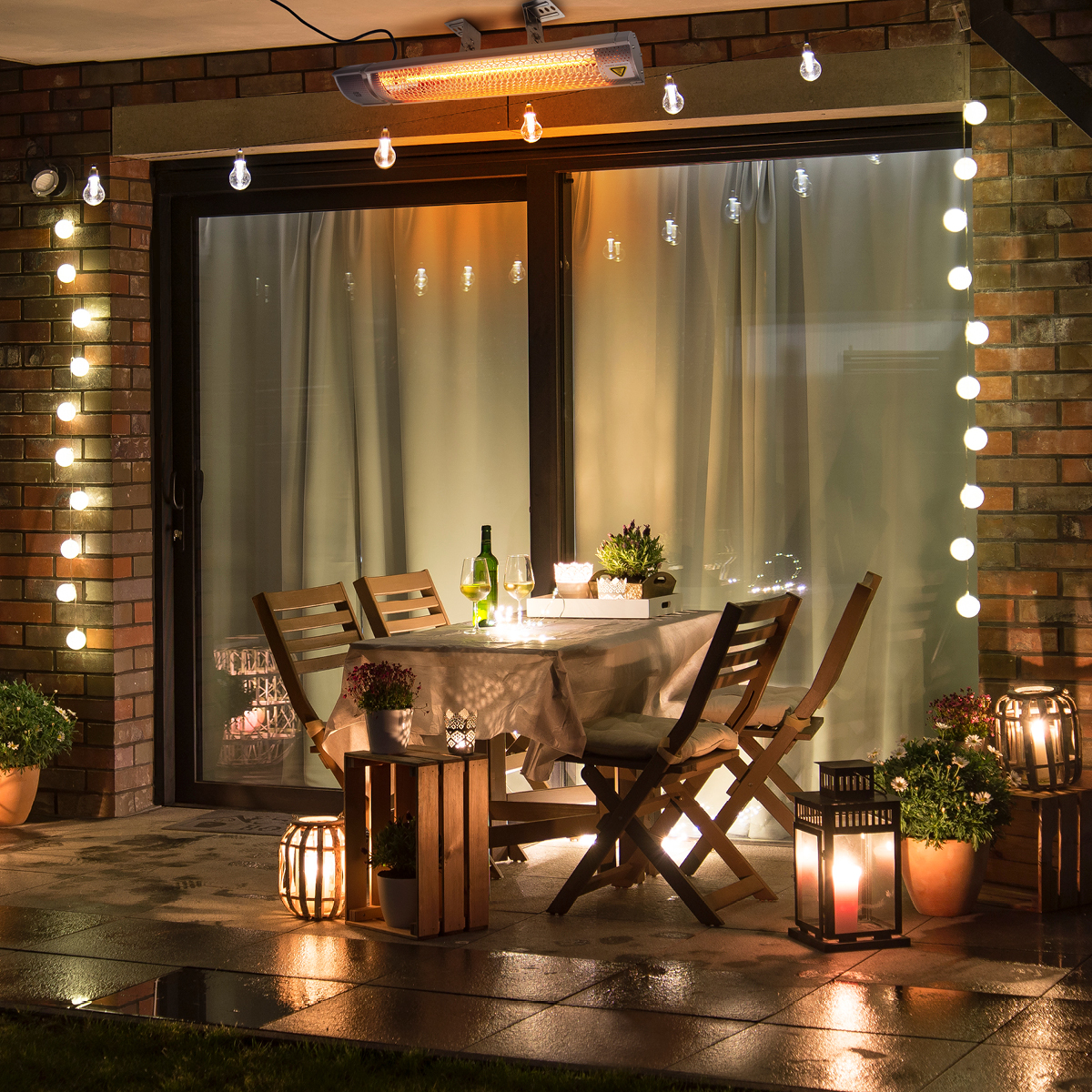 Een patio 's nachts met lichtslingers, tafels, stoelen en planten. Er is een kachel boven de tafel.