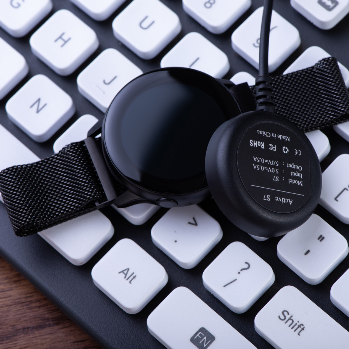 Smartwatch und Ladekabel. Die Uhr ist schwarz. Auf einer Tastatur platziert. Weiße Tasten und schwarzer Hintergrund.