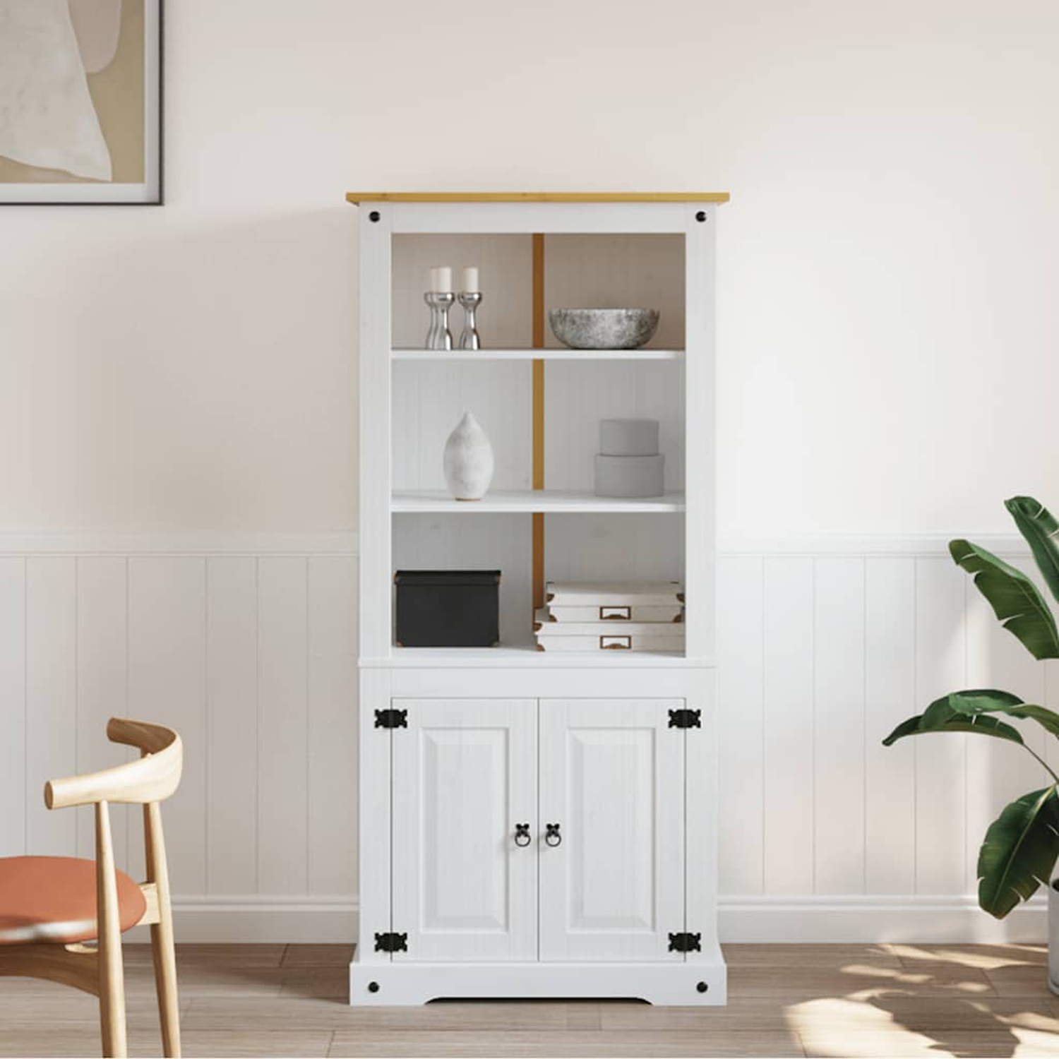 Weißer Schrank mit zwei Türen, Regale mit Gegenständen. Ein Stuhl und eine Pflanze sind im Hintergrund.