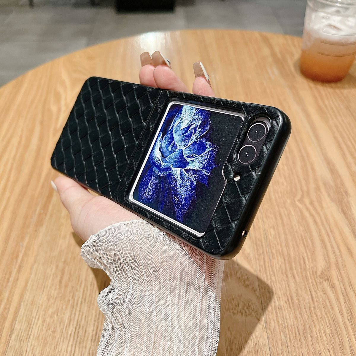 Schwarze Handyhülle mit gewebtem Muster. Das Telefon zeigt einen Bildschirm an. Eine Hand hält die Hülle.