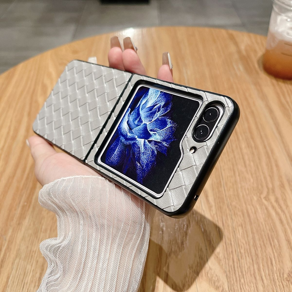 Hand hält ein gefaltetes Telefon mit hellgrauer strukturierter Hülle auf einem Holztisch.