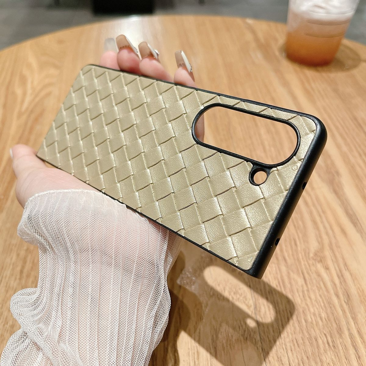 Hand hält eine goldene, gewebte Handyhülle mit schwarzem Rahmen, Draufsicht.