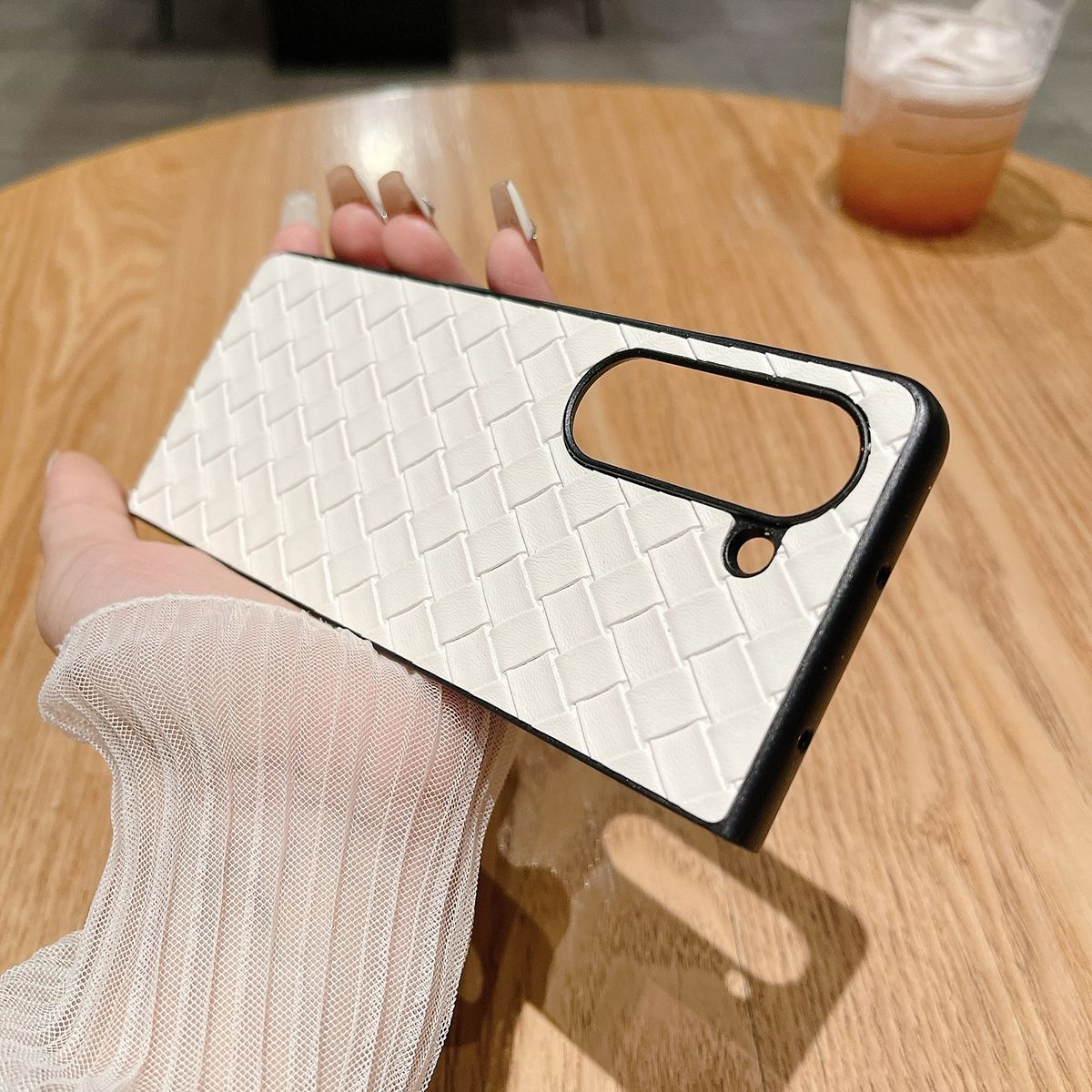 Die Hand einer Person, die eine weiße Handyhülle mit Webmuster auf einem Holztisch hält.