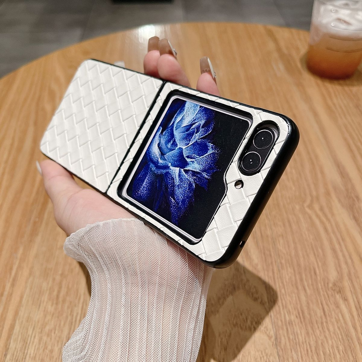 Hand, die eine weiße gewebte Handyhülle mit einem faltbaren Telefon hält, das einen Bildschirm zeigt.