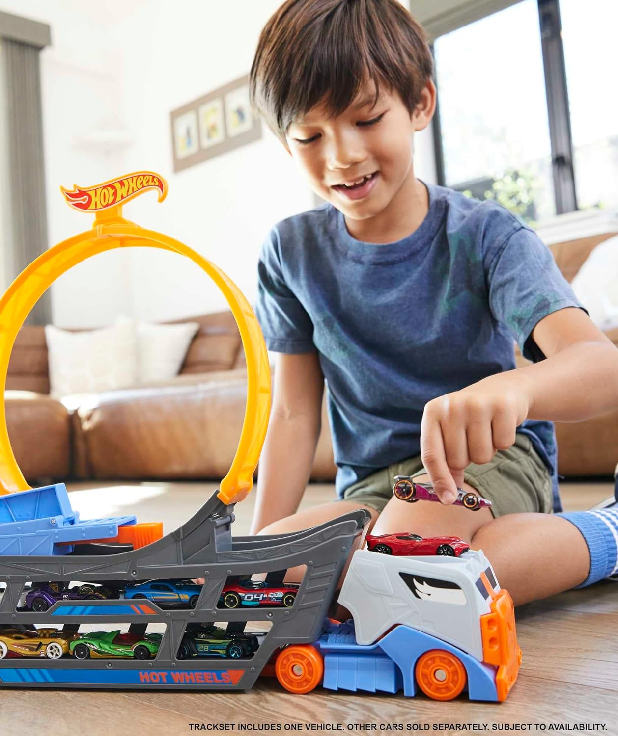 Un garçon joue avec un circuit Hot Wheels avec une boucle. Plusieurs voitures jouets sont visibles.