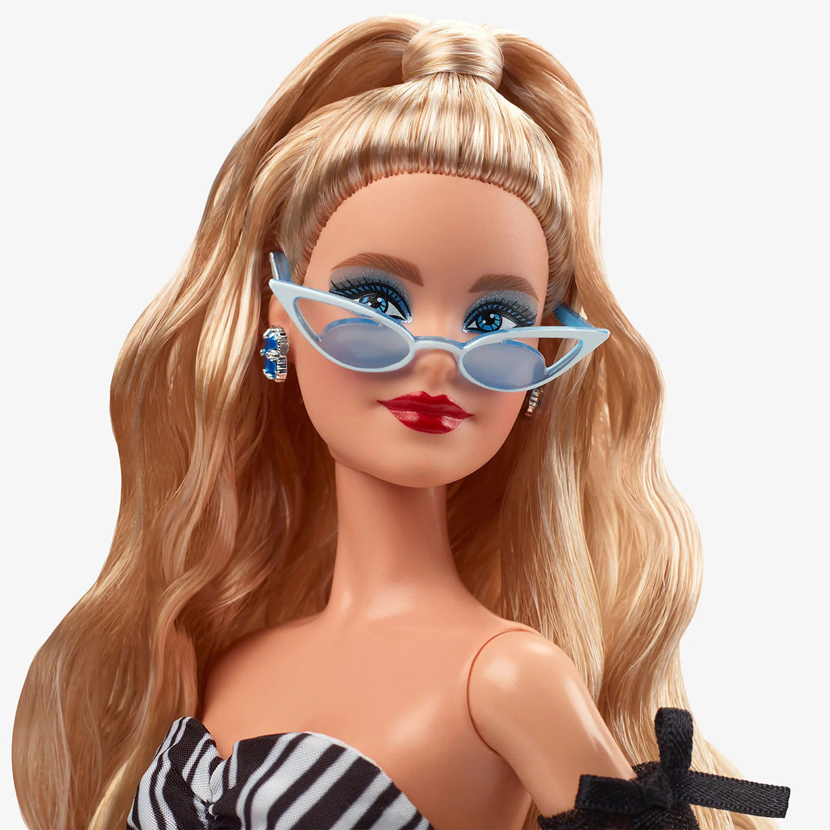 Primer plano de una muñeca Barbie con cabello rubio, ojos azules y gafas de sol. Lleva un top con estampado de cebra.