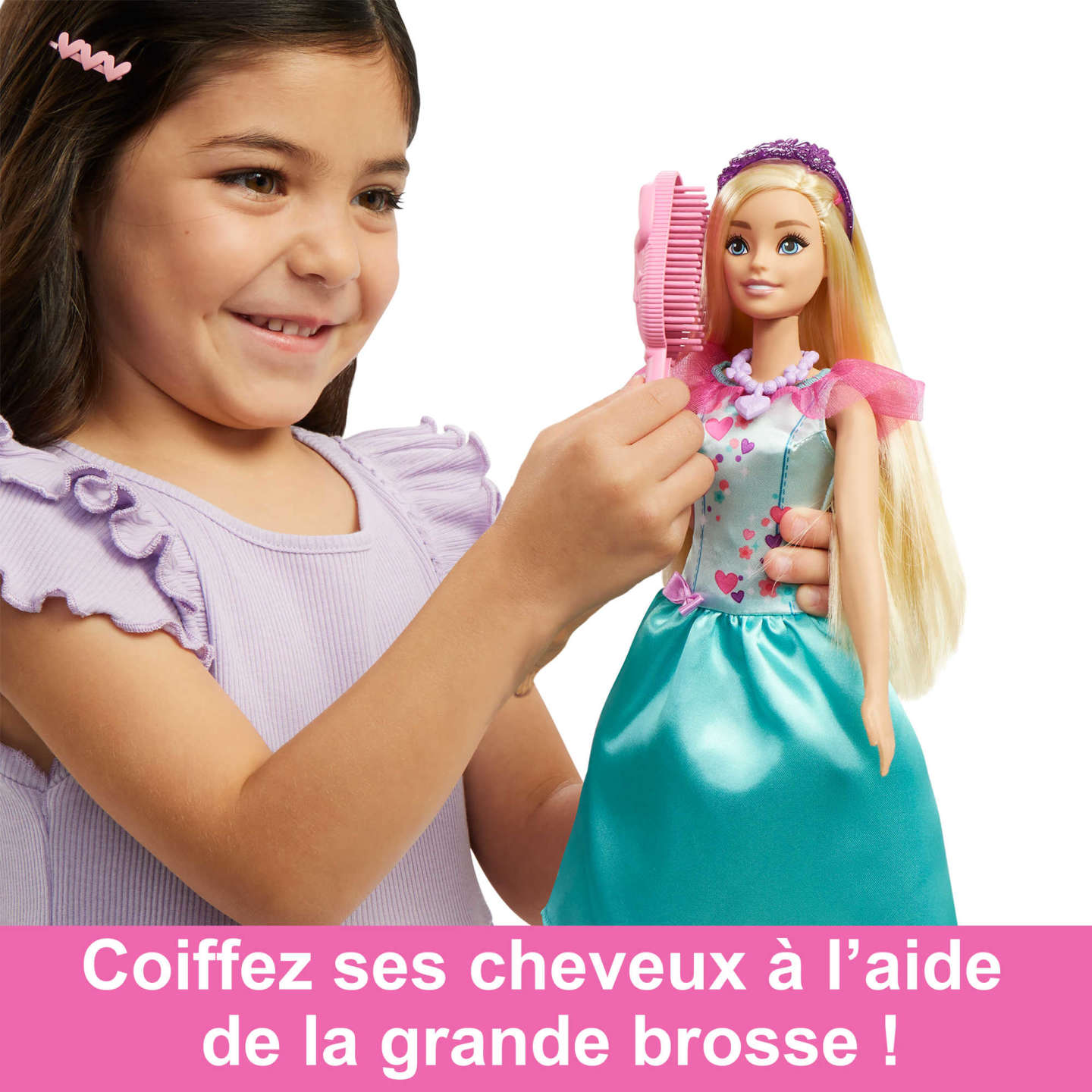 Ein junges Mädchen kämmt das Haar einer Barbie-Puppe mit einer rosa Bürste. Beide lächeln, weißer Hintergrund.