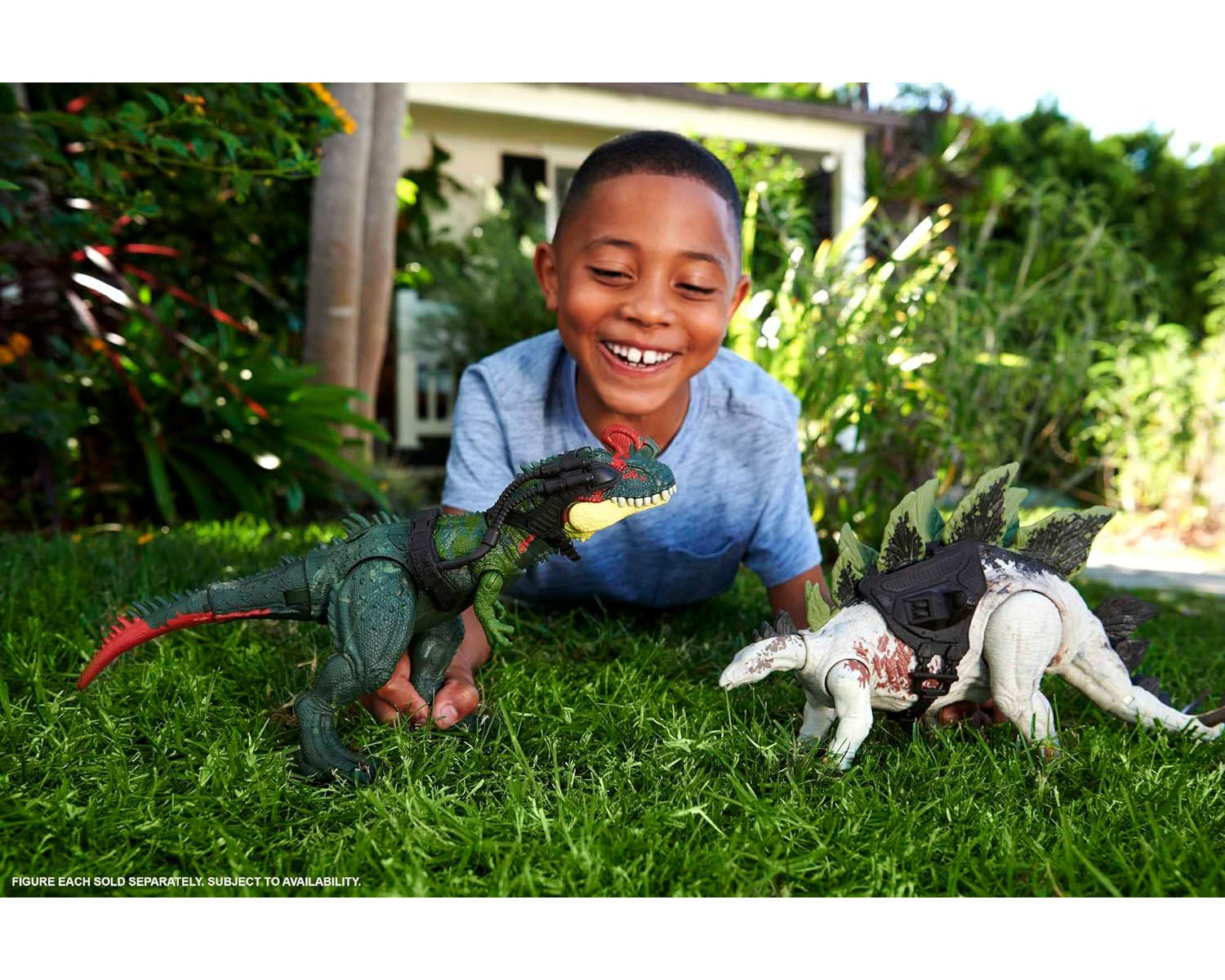 Un ragazzo sorridente gioca con i giocattoli dei dinosauri su un prato verde. I dinosauri hanno selle e sono in battaglia.