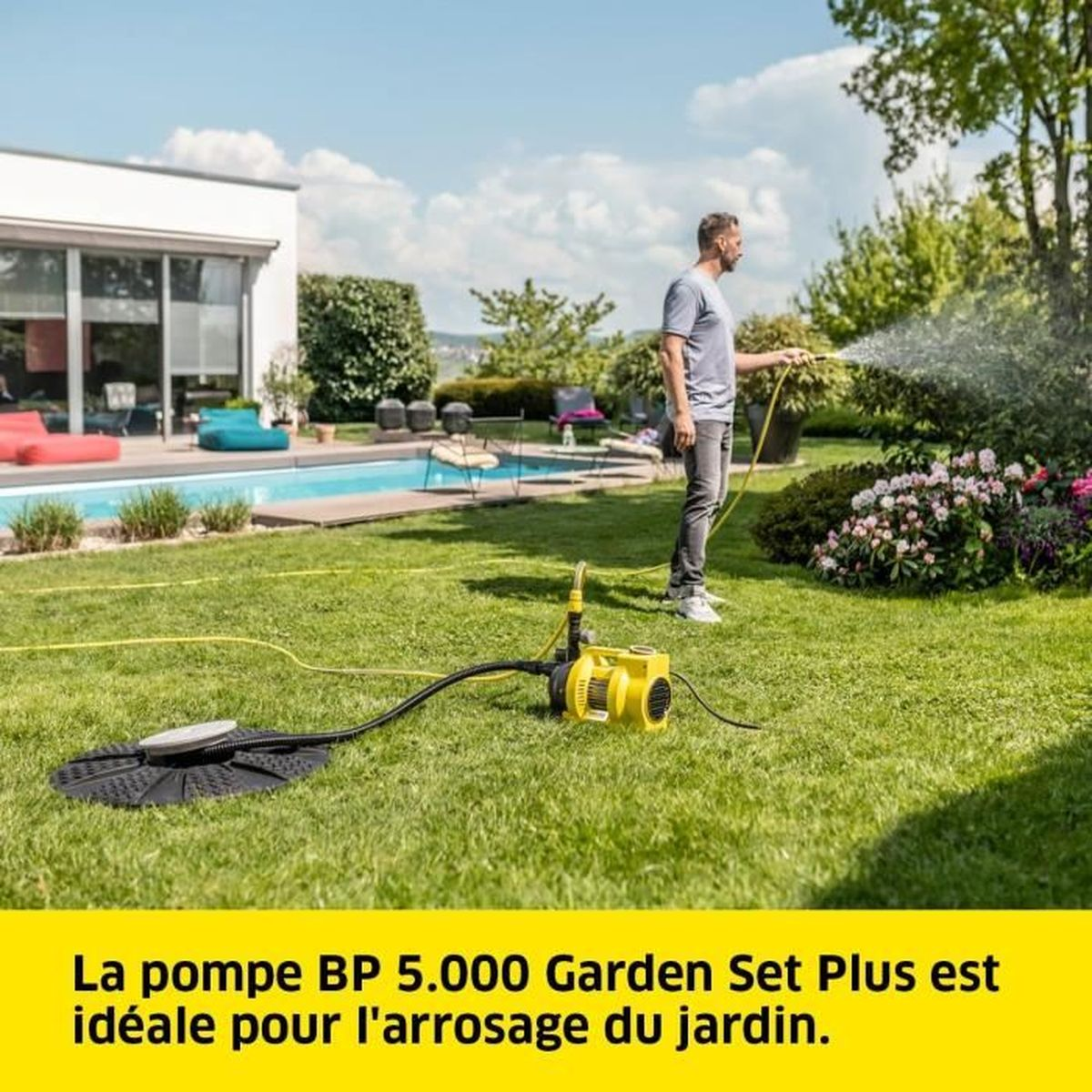 Ein Mann bewässert einen Garten mit einer gelben Pumpe auf dem Rasen. Im Hintergrund sind ein Haus und ein Pool.