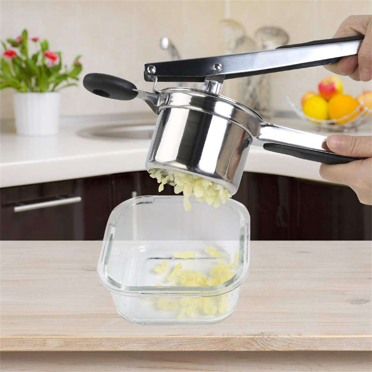 Eine Person zerdrückt Kartoffeln mit einem Kartoffelstampfer in eine Glasschüssel.