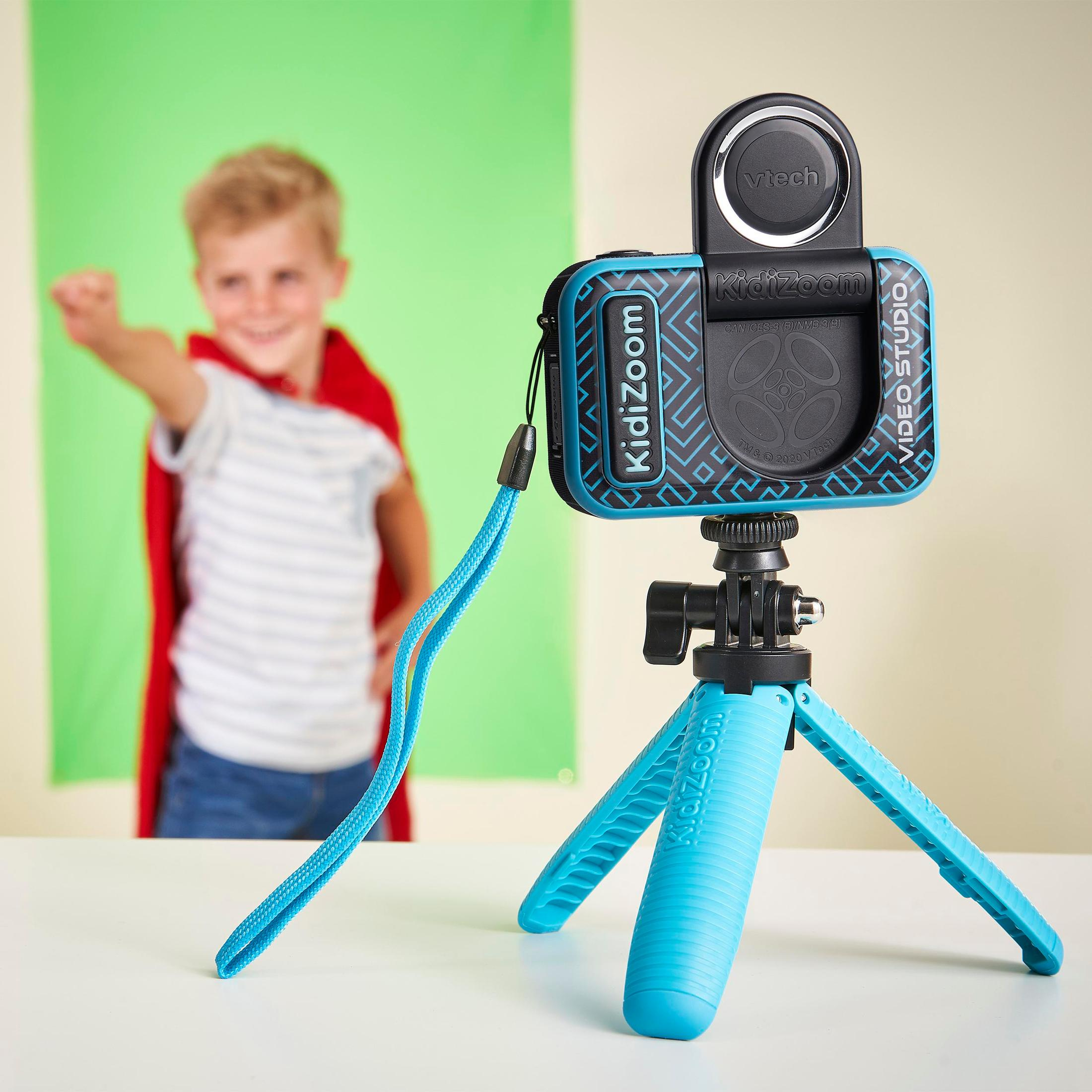 Eine Kidizoom Video Studio Kamera auf einem Stativ, mit einem Kind im Hintergrund, das mit einem Umhang fliegt.