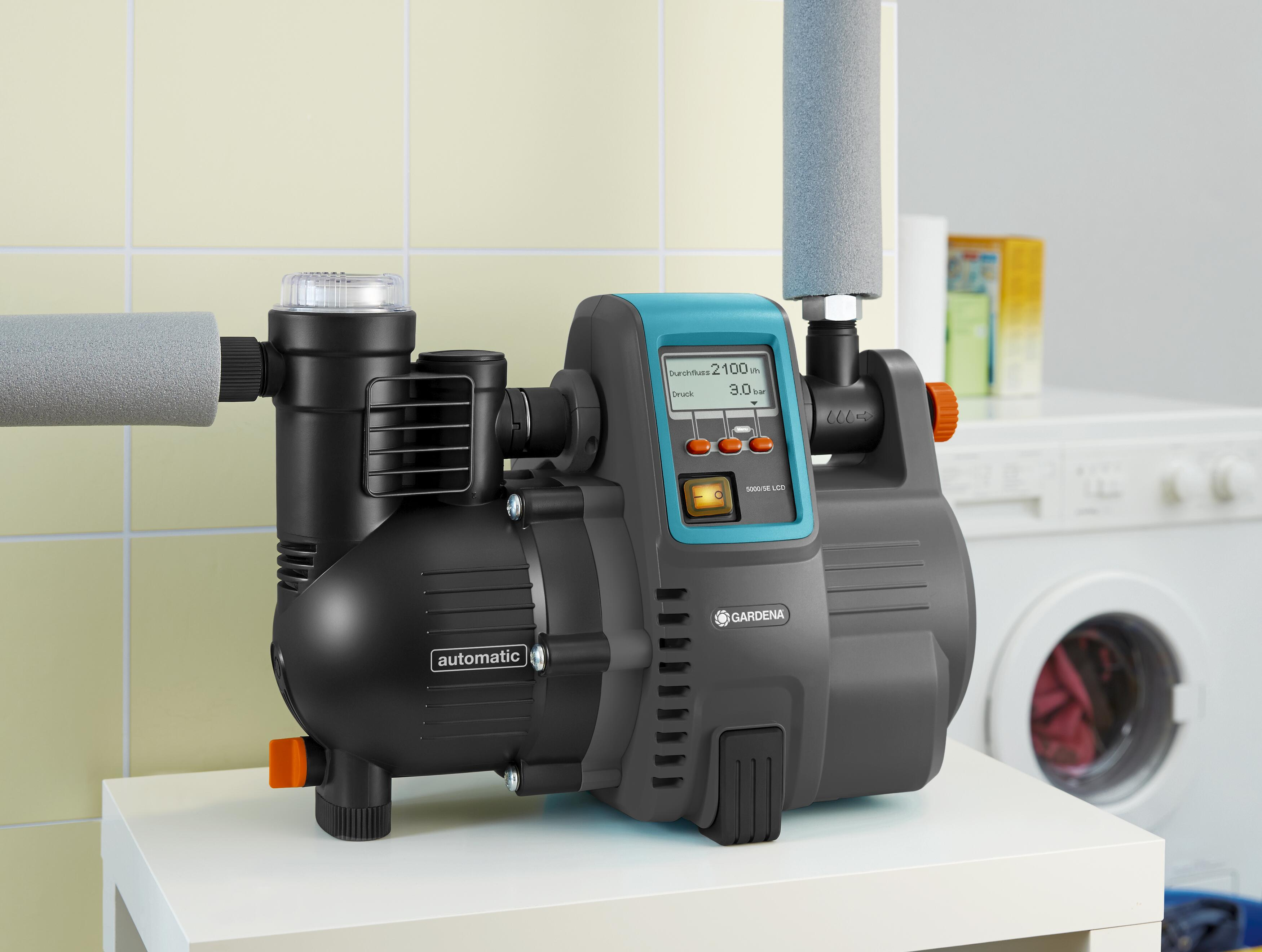 Wasserpumpe mit Digitalanzeige, angeschlossen an Rohre. Es steht auf einer weißen Oberfläche.