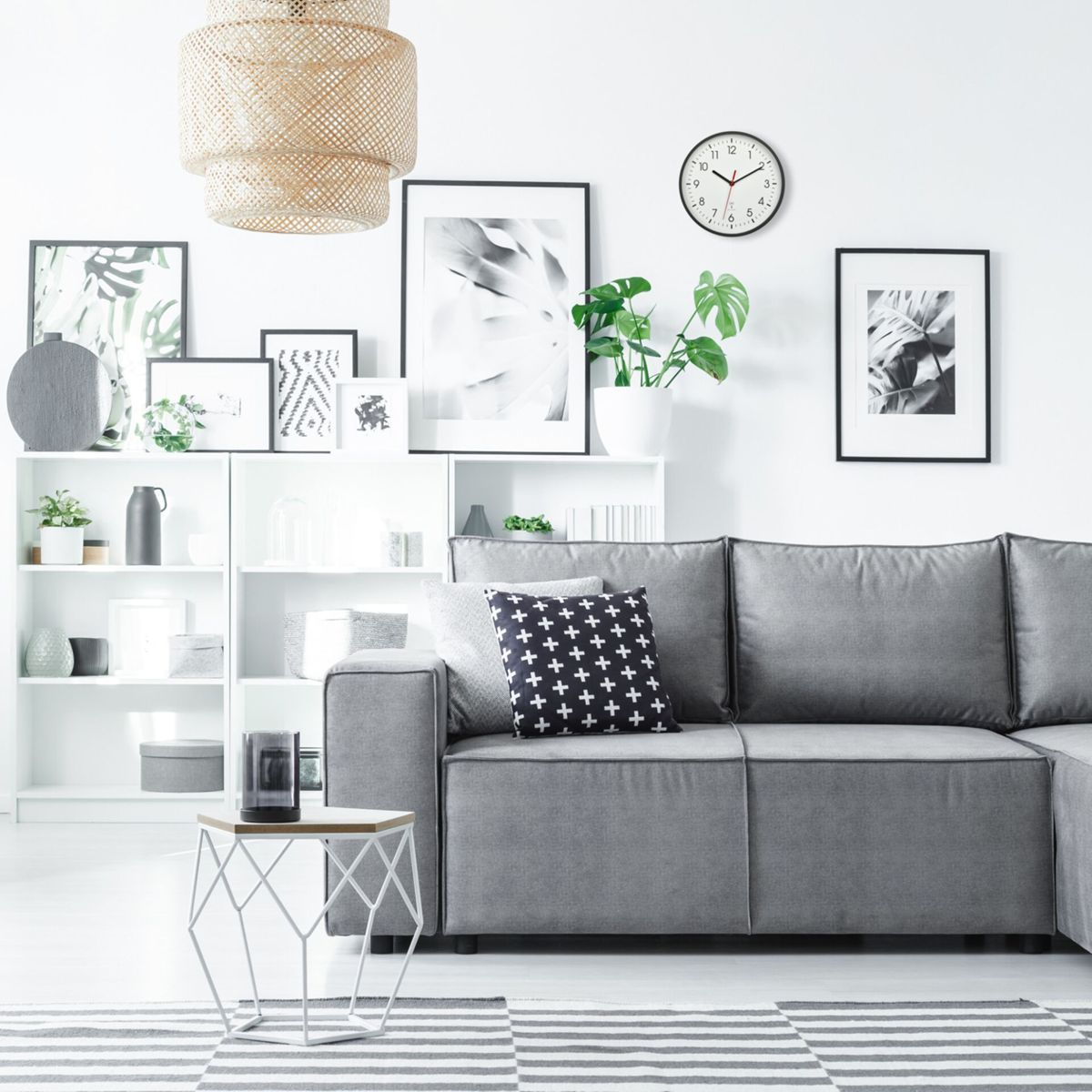 Salon avec un canapé gris, des étagères blanches, des tableaux et un tapis rayé.