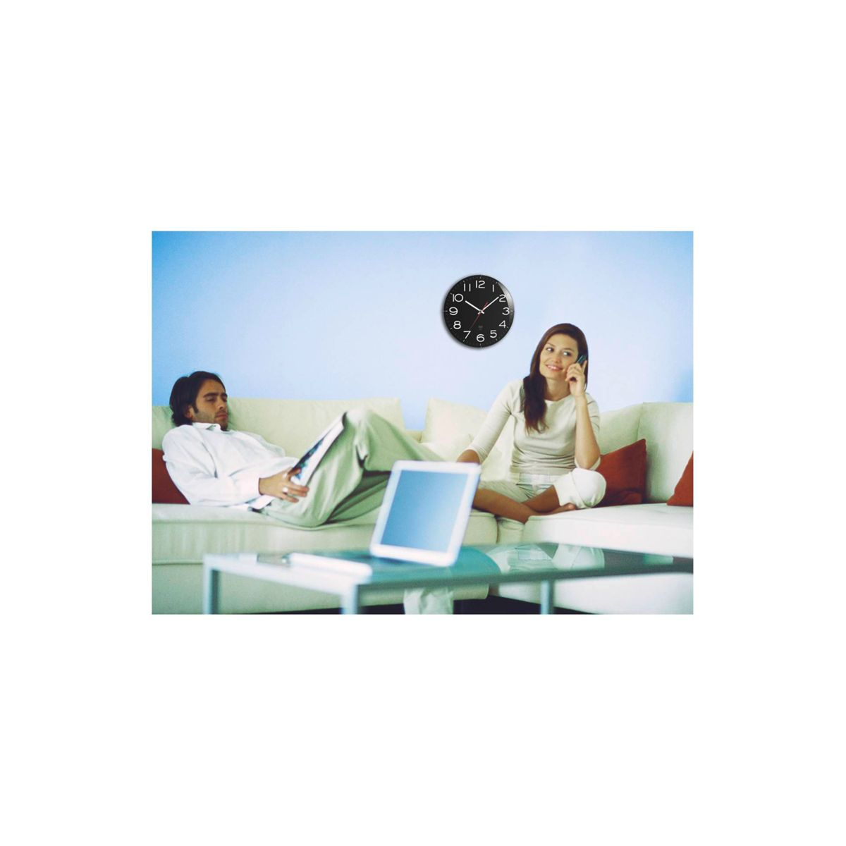 Ludzie na sofie, zegar na ścianie i laptop na stole.