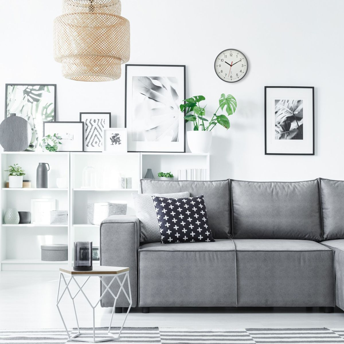 Wohnzimmer mit grauem Sofa, weißen Regalen mit Dekorationen, Bildern an der Wand und einem gestreiften Teppich.