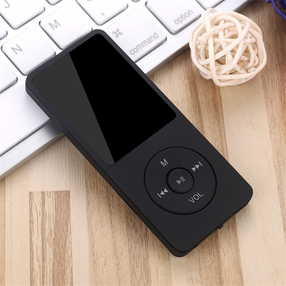 Schwarzer MP3-Player auf einem Holztisch, mit einer weißen Tastatur und einer weißen Kugel im Hintergrund.