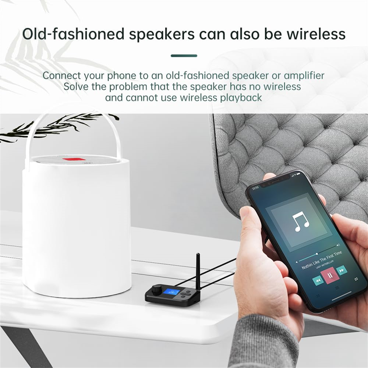 Ein weißer Lautsprecher mit einem schwarzen Empfänger steht auf einem Tisch. Eine Hand hält ein Telefon.