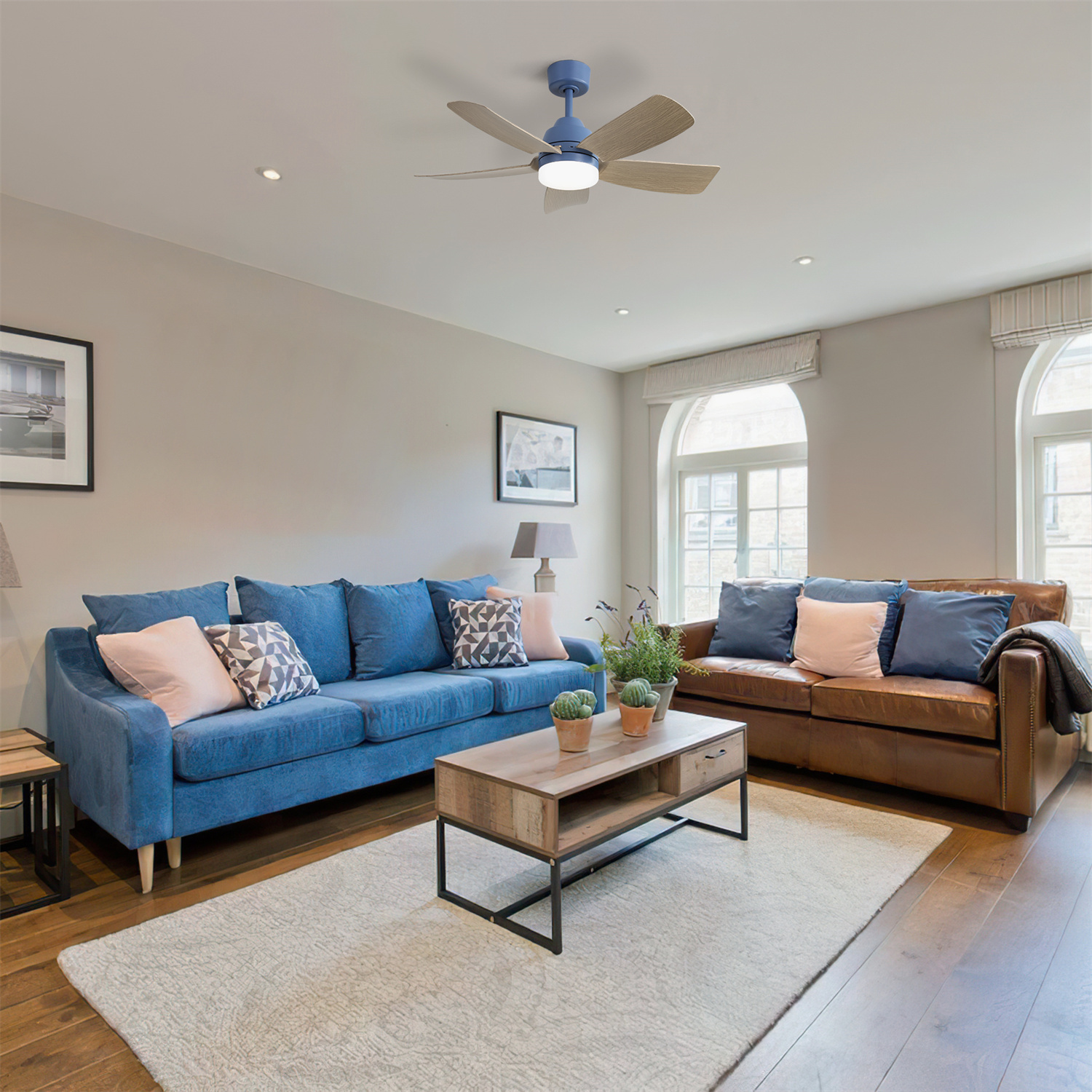 Ein Wohnzimmer mit blauen und braunen Sofas. Es gibt einen Deckenventilator. Ein Couchtisch und ein Teppich sind im Raum.