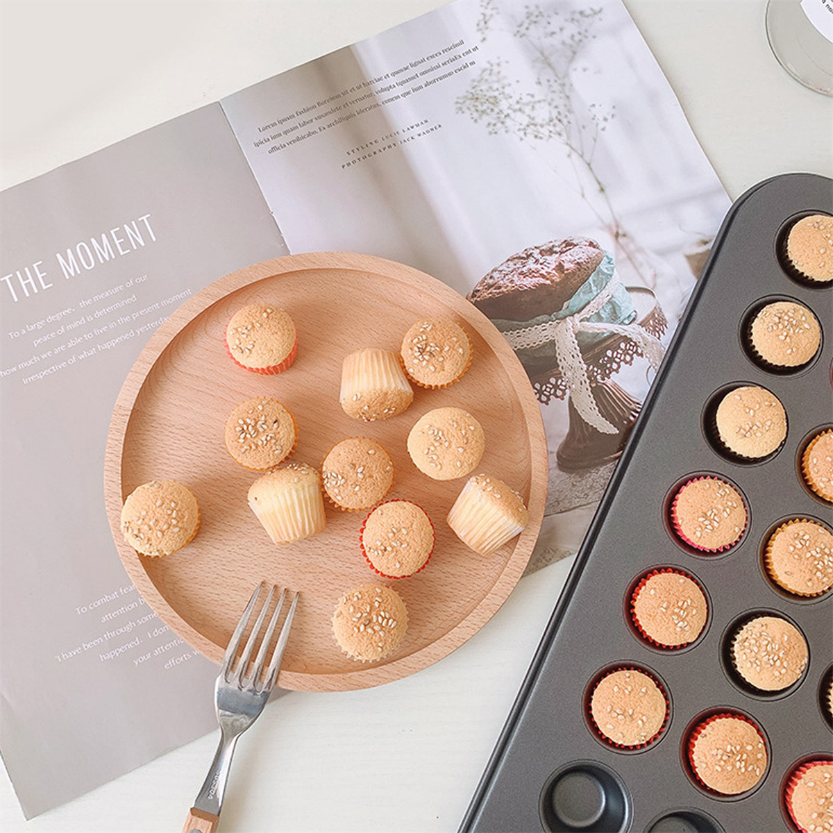 Holzteller mit Cupcakes. Backblech mit Cupcakes rechts. Magazin im Hintergrund.
