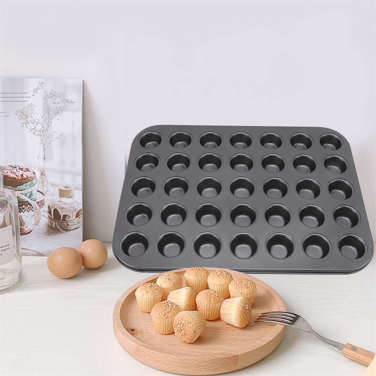 Ein Backblech mit Muffinförmchen, mit fertigen Muffins auf einem Holzbrett und Eiern.