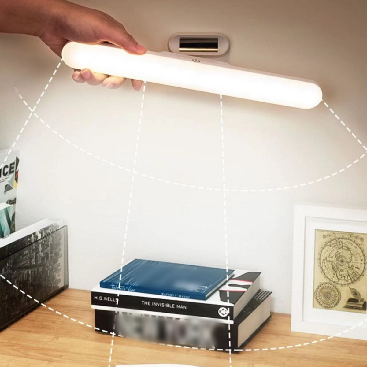 Eine Hand hält ein weißes LED-Licht über einem Schreibtisch mit Büchern und einem Bilderrahmen.