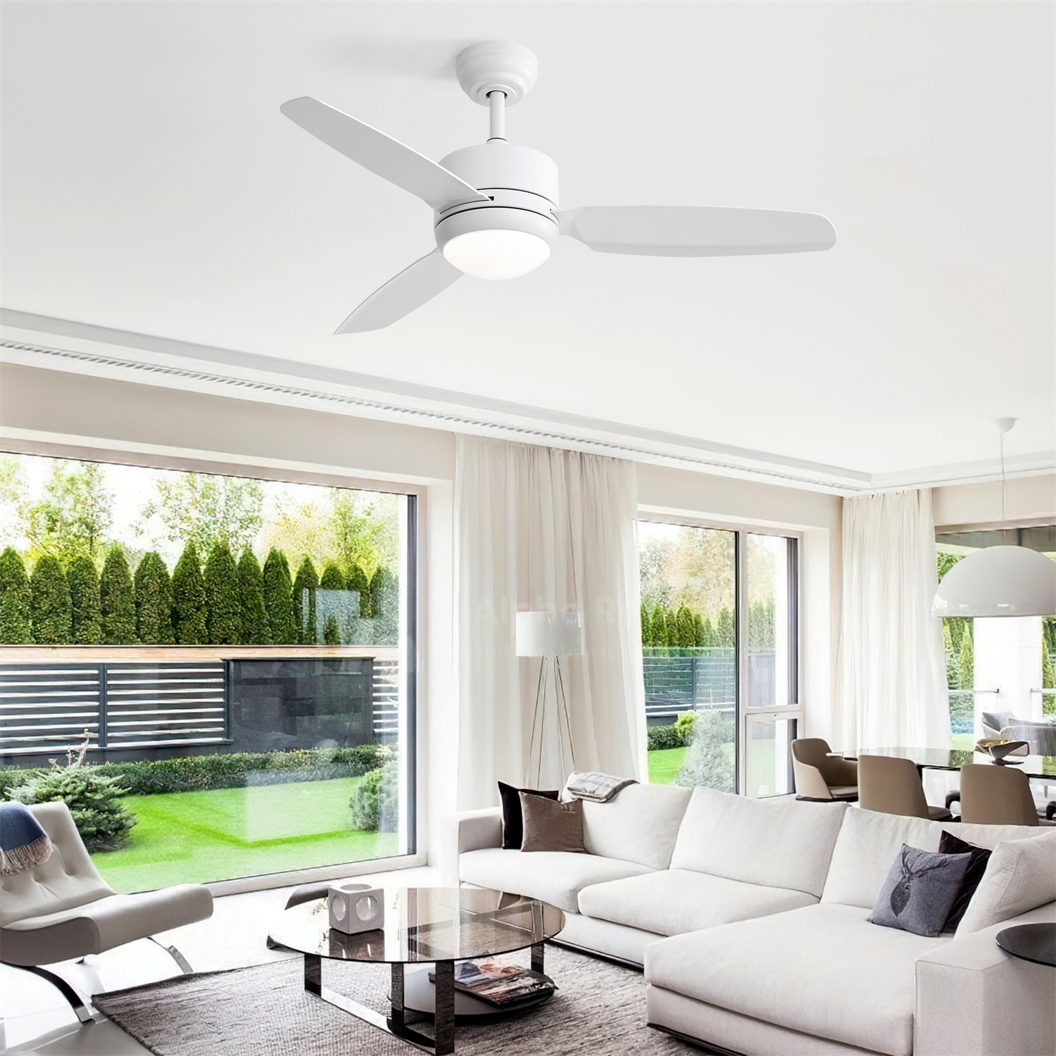 Weißer Deckenventilator mit drei Flügeln. Wohnzimmer mit weißen Möbeln, großen Fenstern und Grün draußen.