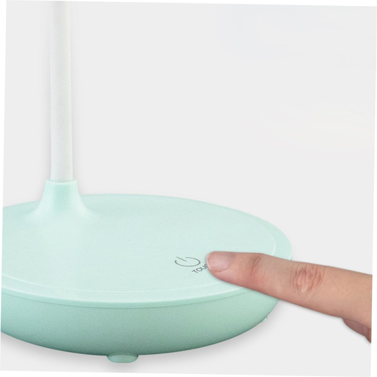 Eine Hand drückt die Touch-Taste auf einer mintgrünen Schreibtischlampe.