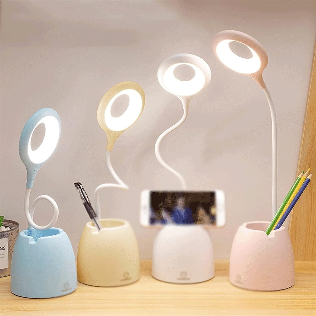 Vier Schreibtischlampen mit Telefonhaltern, Stiften und Bleistiften auf hellem Hintergrund.