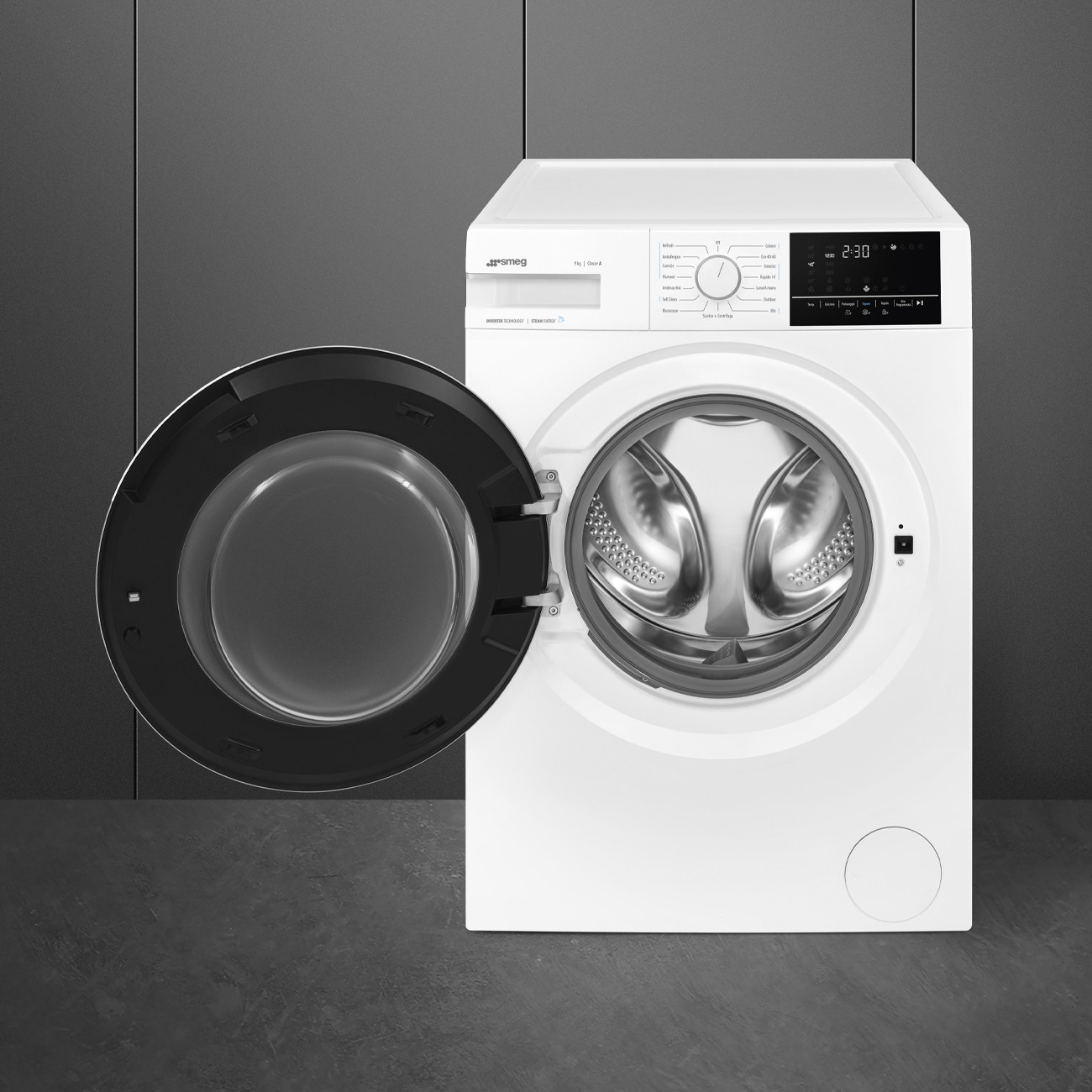 Una lavatrice Smeg bianca con la porta aperta, su una superficie grigia. Lo sfondo è grigio.
