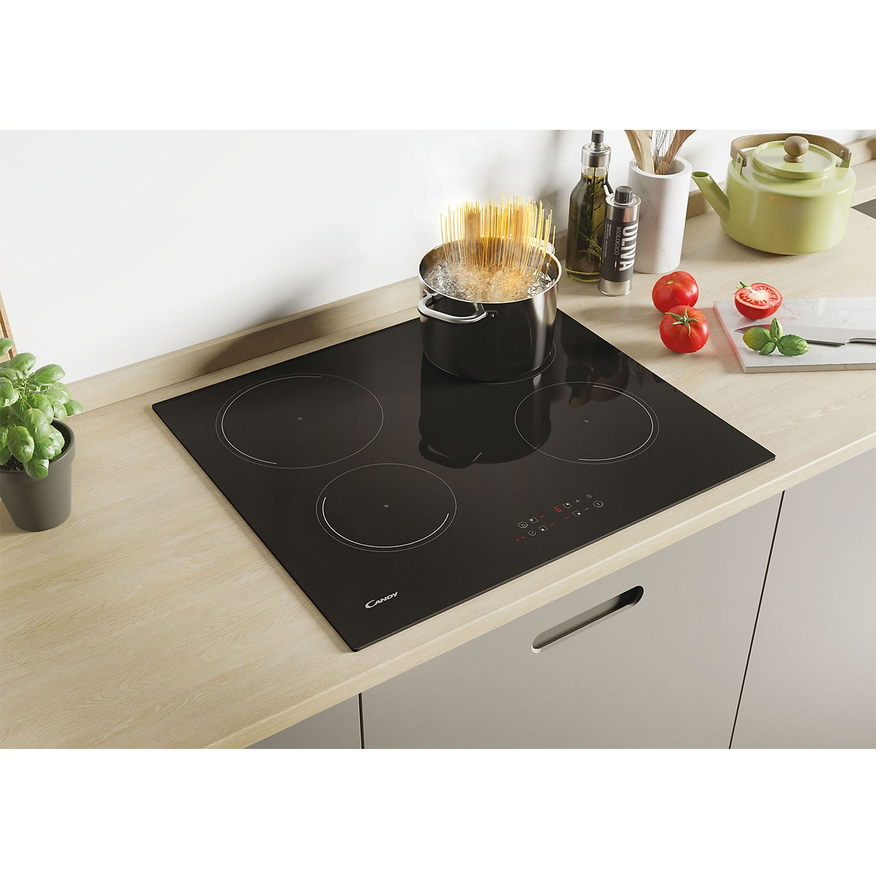 Czarna płyta grzewcza z czterema palnikami. Wrząca woda w garnku. Pomidory i oliwa z oliwek. Drewniany blat.