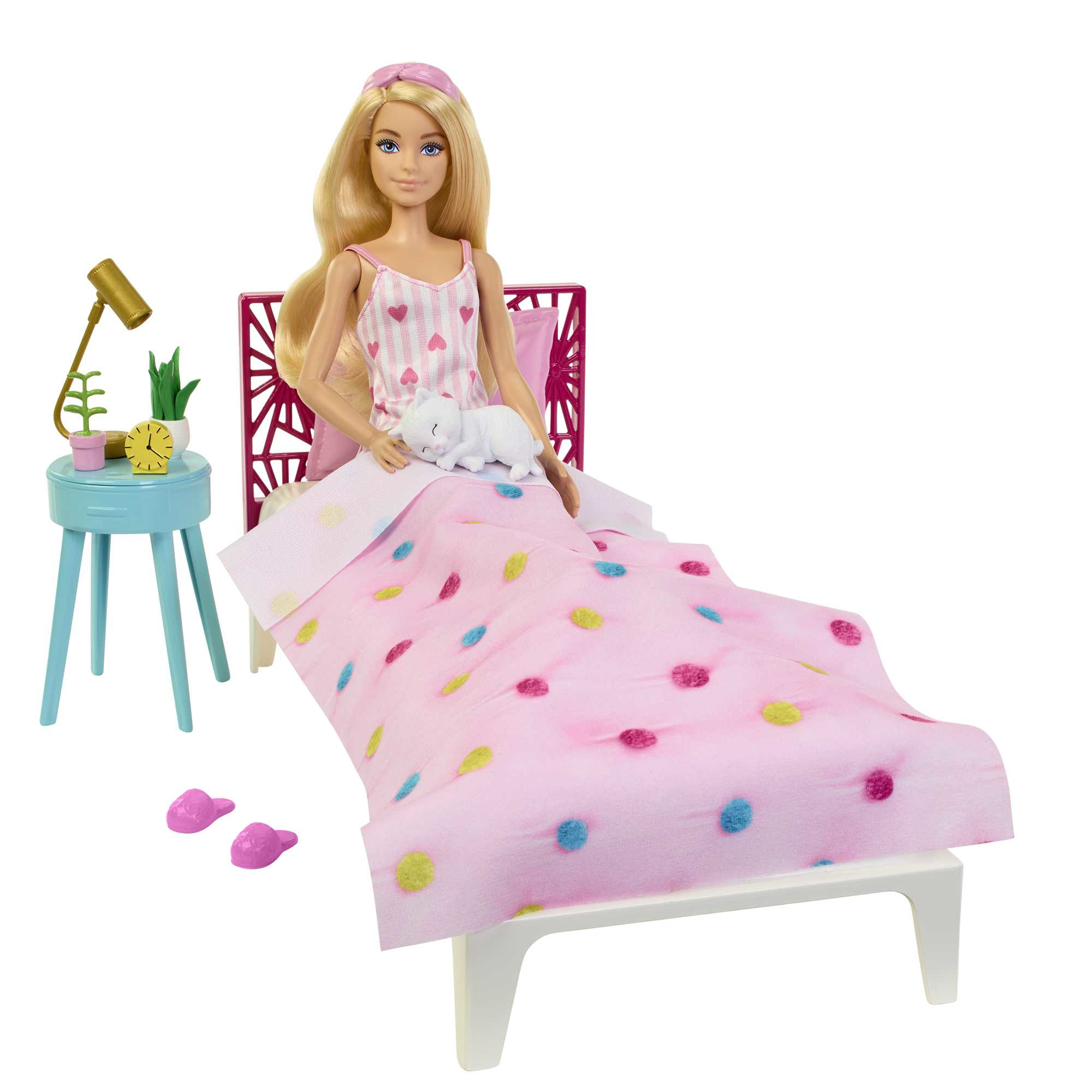 Una muñeca Barbie sentada en una cama con accesorios como una lámpara y zapatillas.