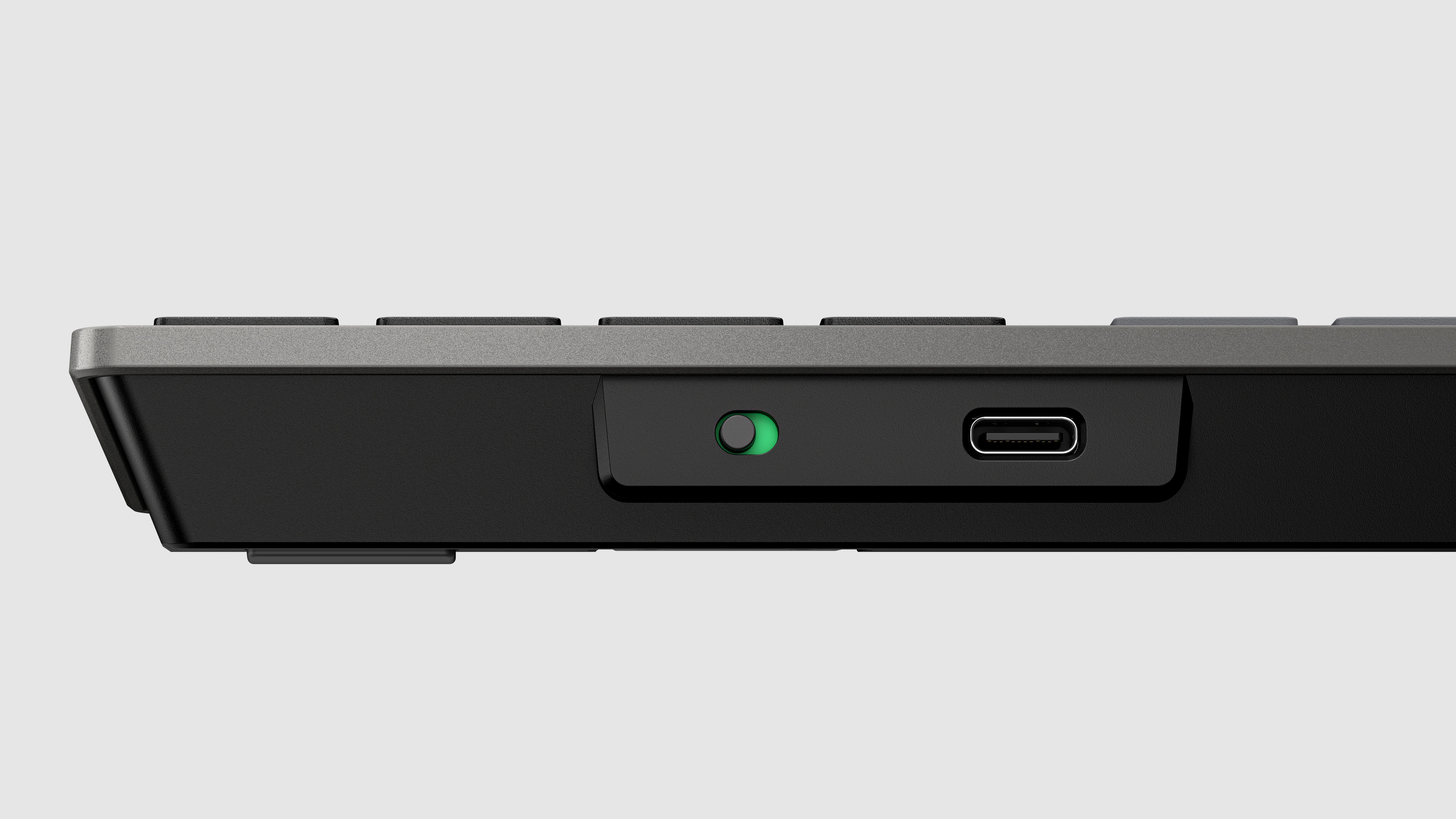 Vista laterale di una tastiera nera con pulsante di accensione verde e porta USB-C, su superficie grigia.