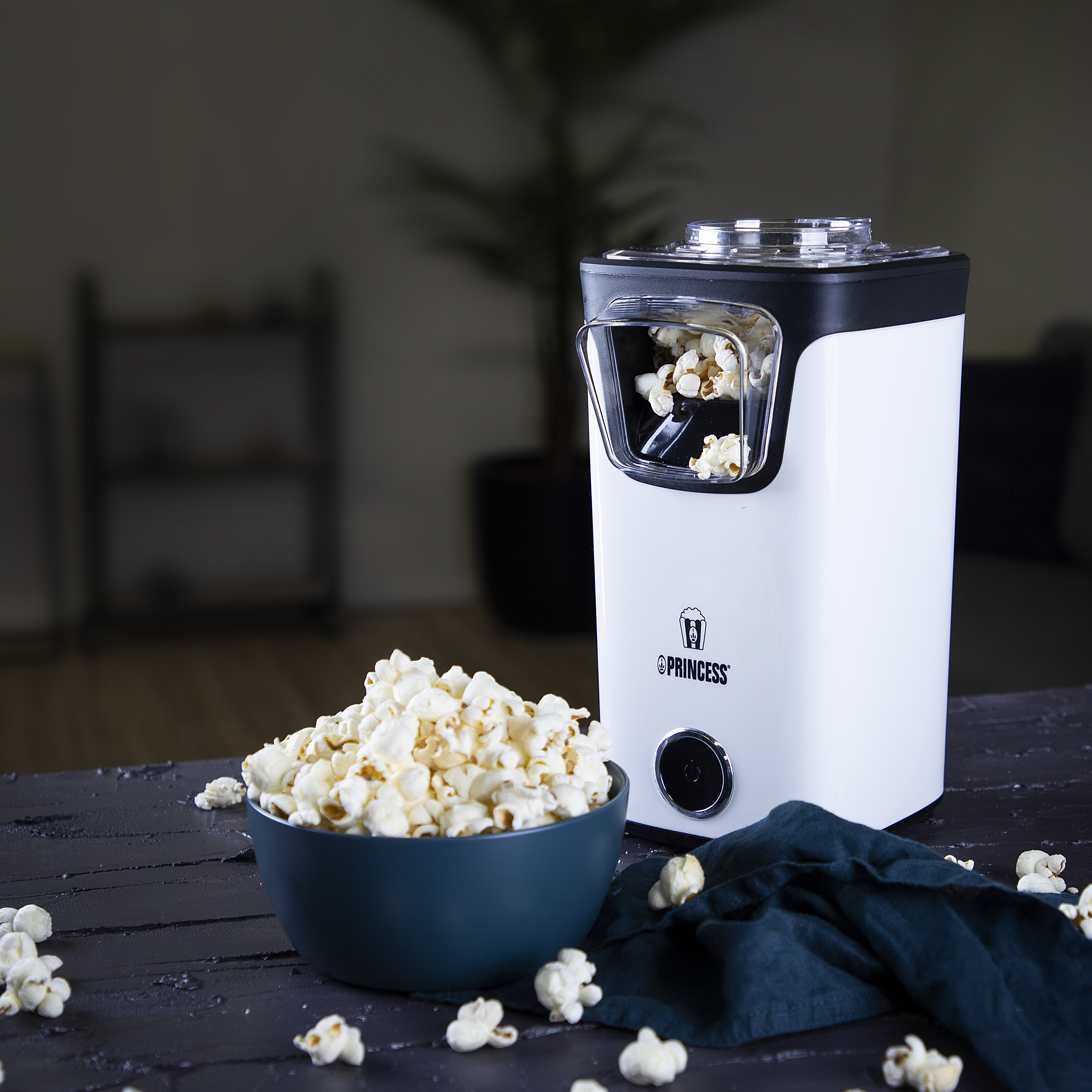 Macchina per popcorn su una superficie scura. Macchina bianca e nera con ciotola di popcorn e chicchi sparsi.
