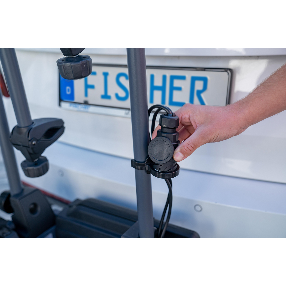 Die Hand einer Person verbindet einen Stecker mit einem Fahrradträger für das Auto. Hintergrund ist ein Auto.