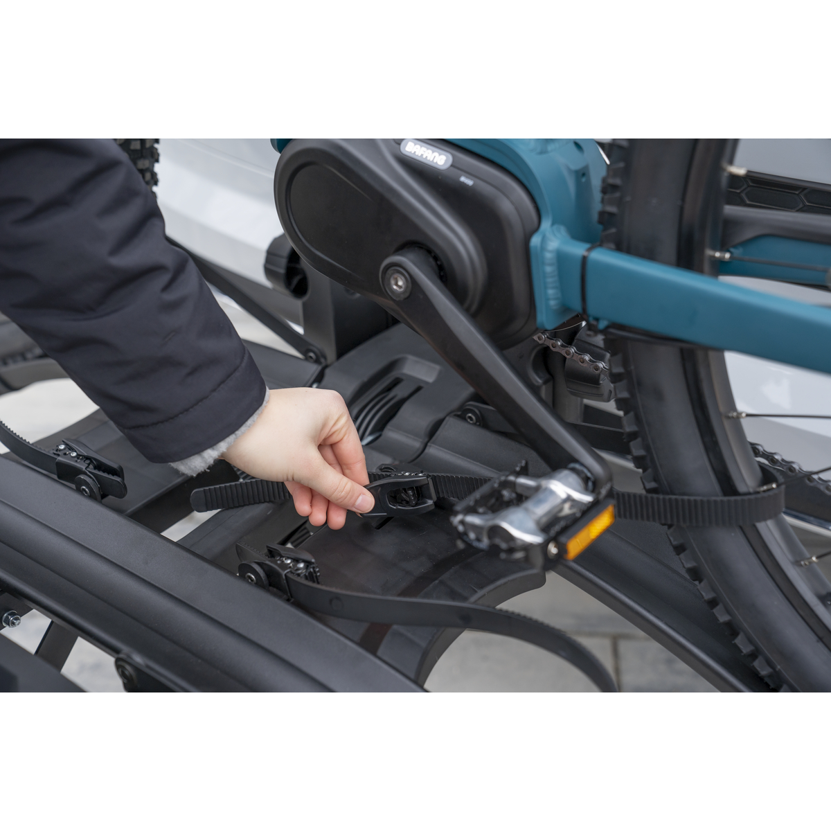 Hand sichert Fahrradriemen am Fahrradträger. Schwarzer Träger, Fahrrad und Hintergrund.