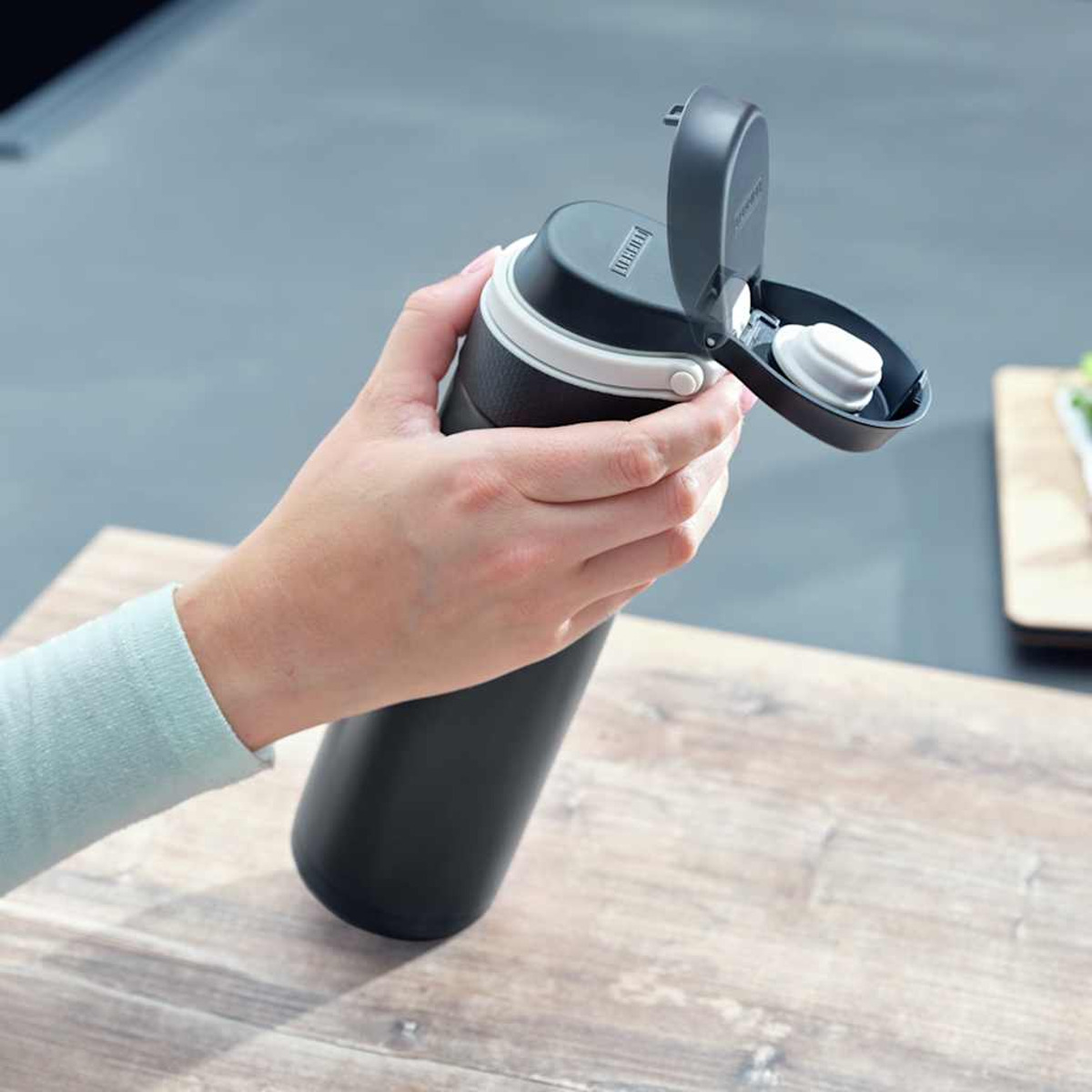 Eine Hand hält eine schwarze Wasserflasche mit weißem Band.