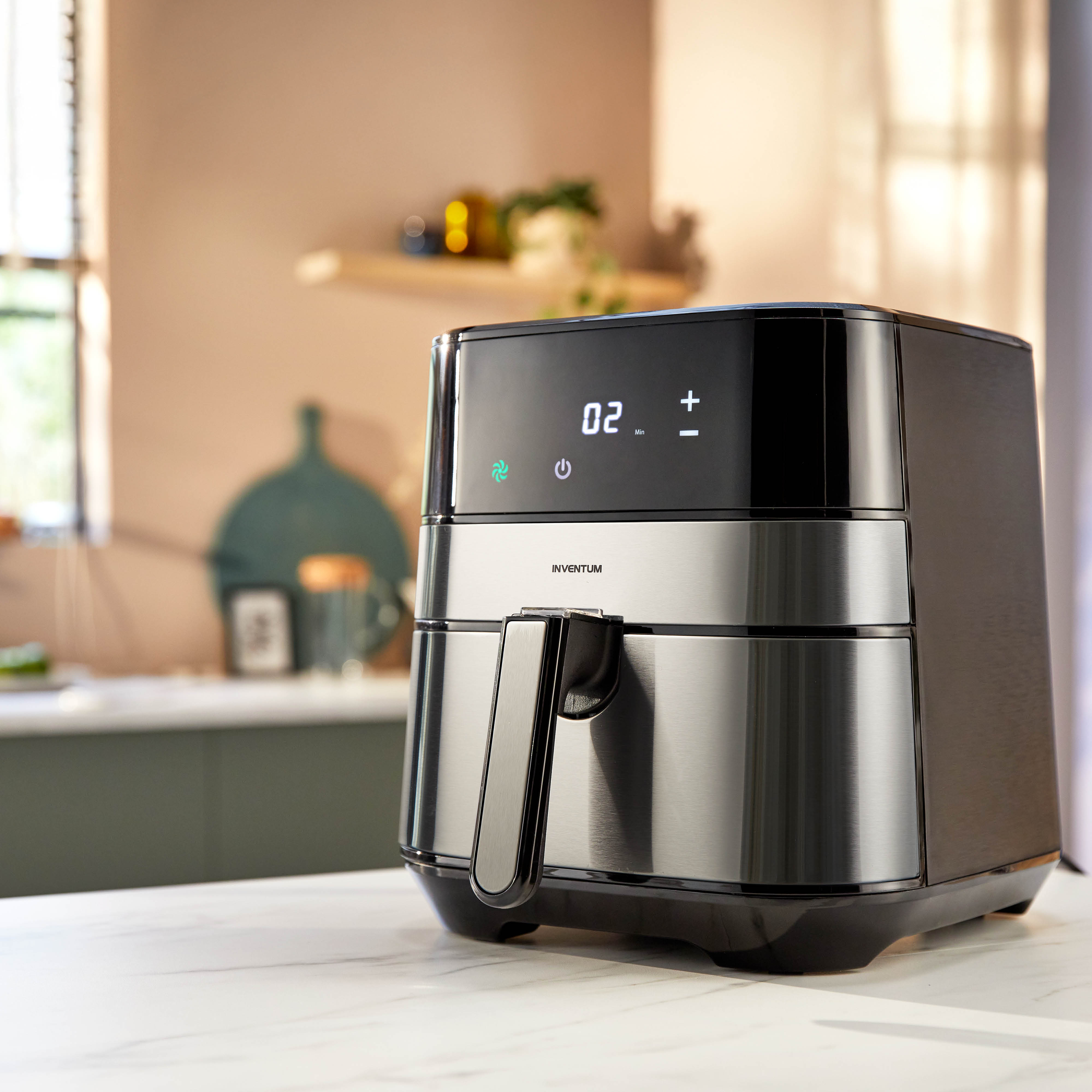 A black and silver air fryer on a white countertop, kitchen background visible.
