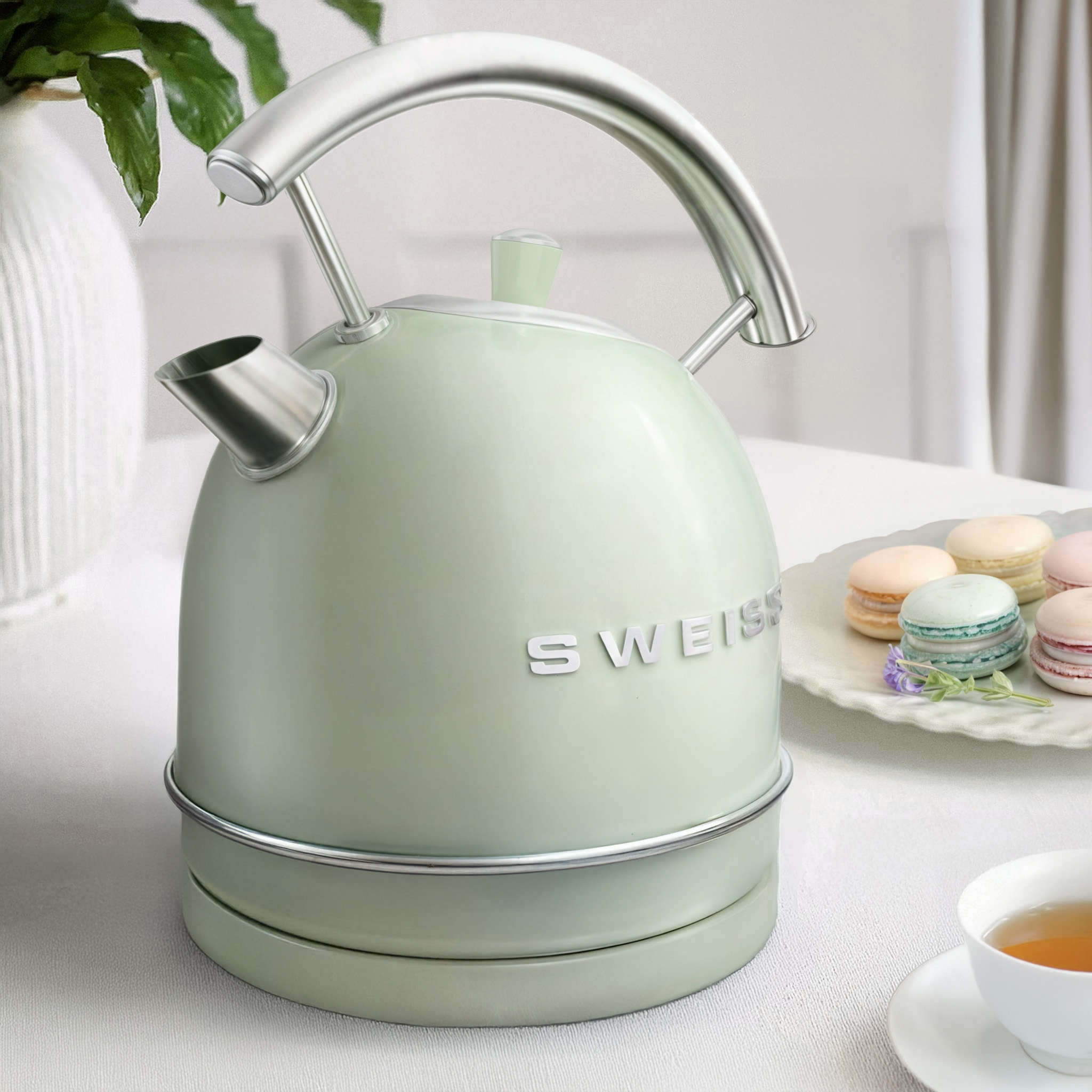 Hervidor verde con asa cromada, texto blanco y macarons sobre una superficie blanca.