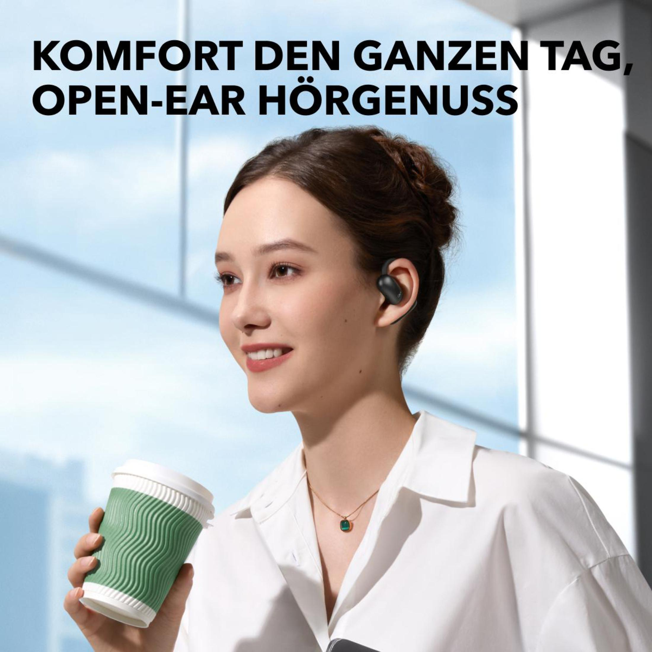 Una mujer con auriculares, sonriendo y sosteniendo una taza de café verde.