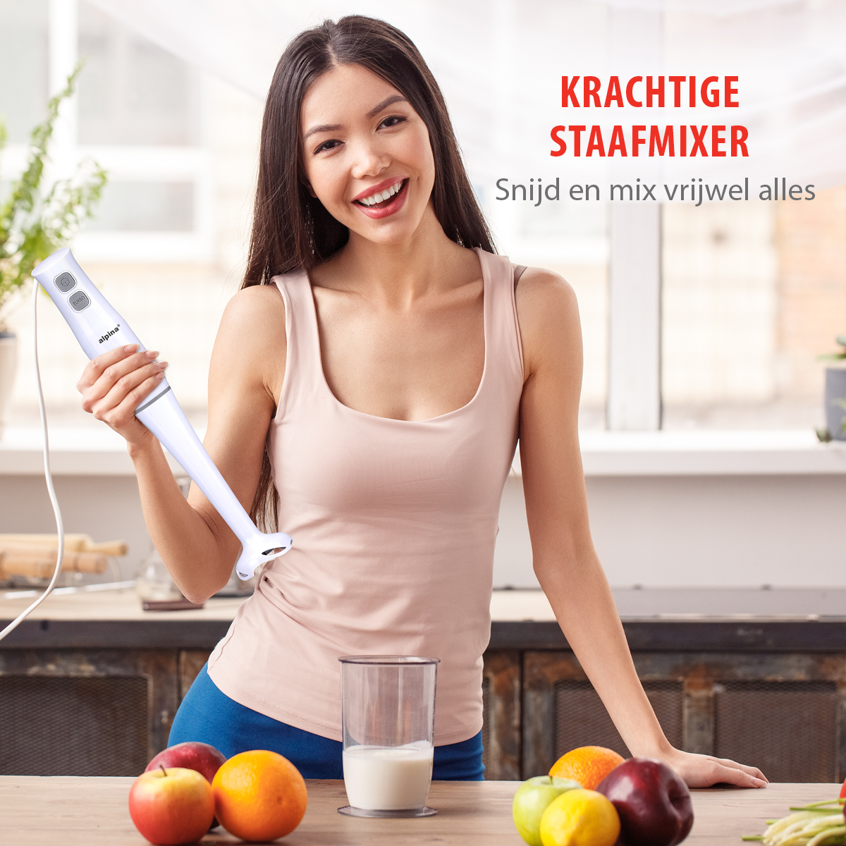 Een vrouw houdt een witte staafmixer vast. Fruit en een glas melk staan op de tafel.