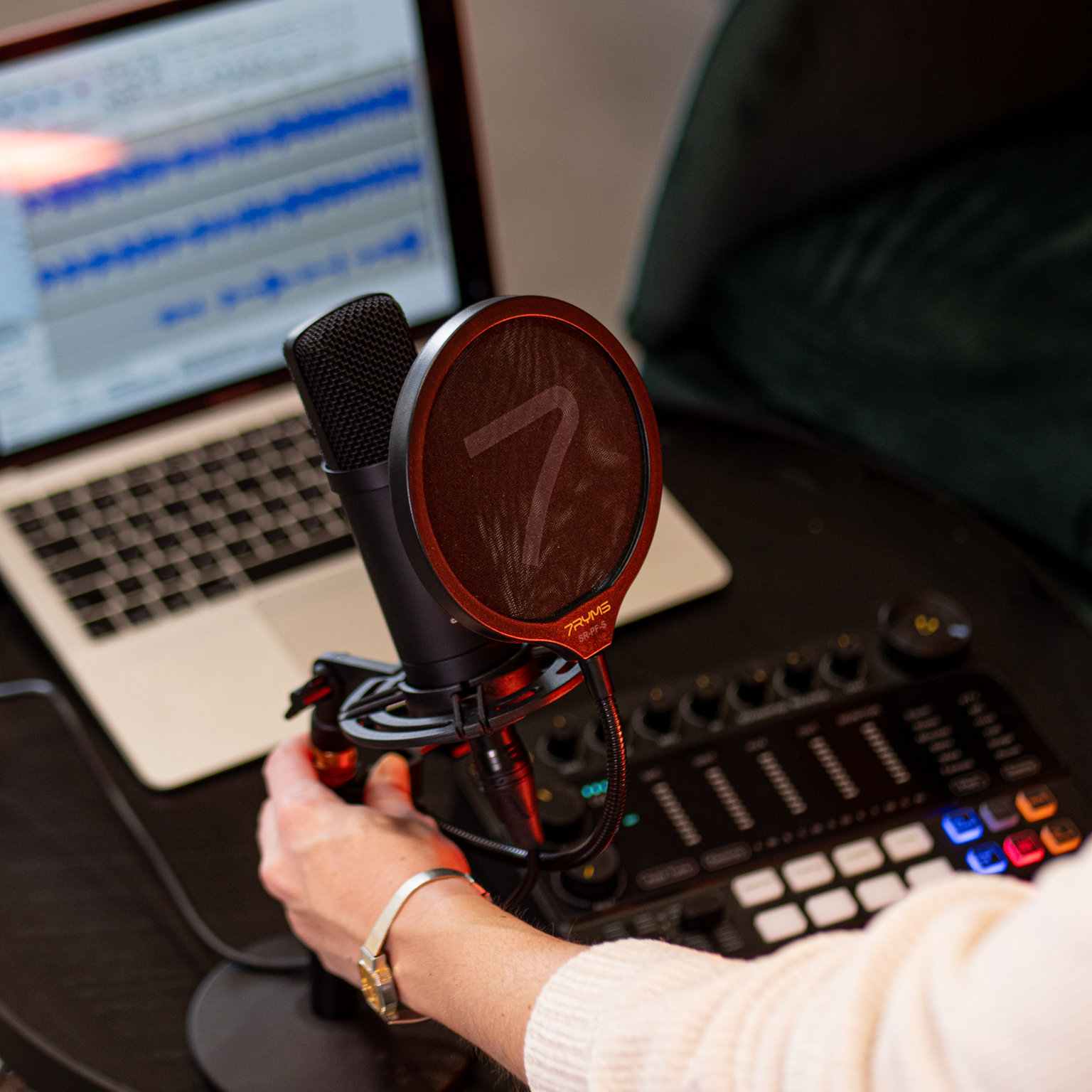 Un microphone avec un filtre anti-pop est sur une table. Un ordinateur portable et une table de mixage sont derrière.