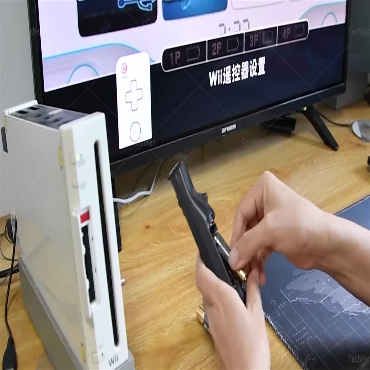 Eine Person legt Batterien in einen schwarzen Gamecontroller ein. Eine Wii-Konsole und ein Fernseher sind im Hintergrund.