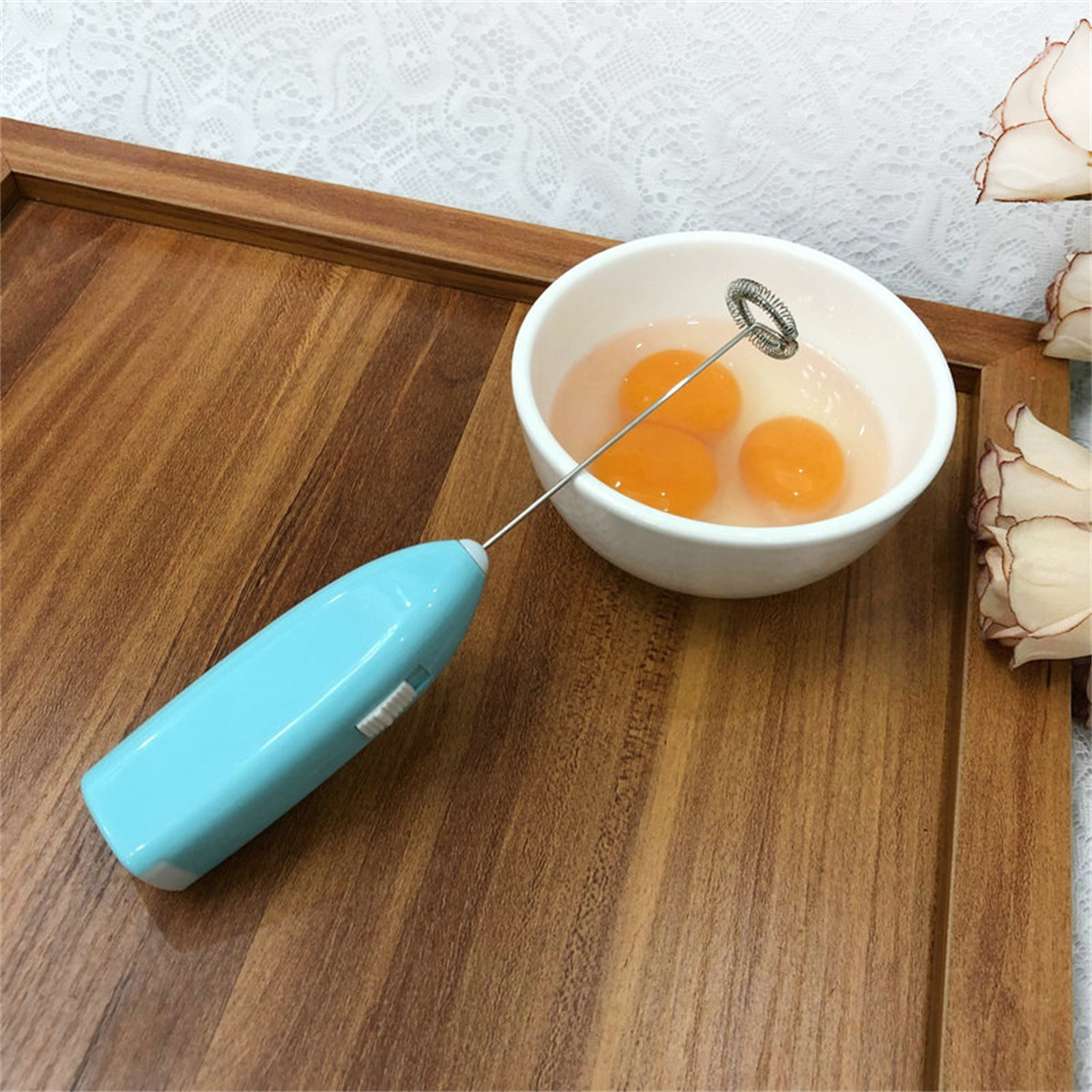Ein blauer Hand-Eierschläger neben einer Schüssel mit Eiern auf einer Holzoberfläche.
