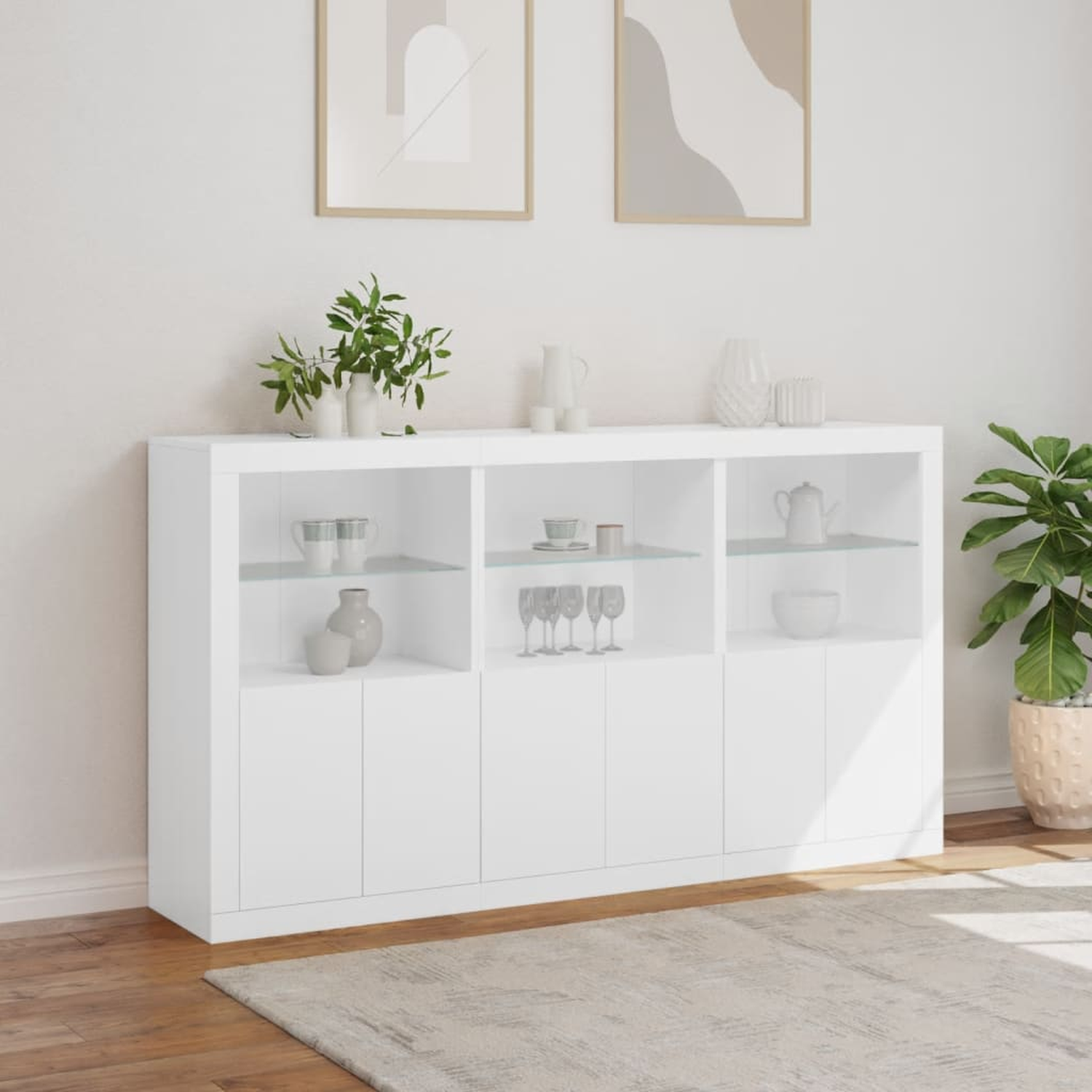Weißer Schrank mit Glasböden. Zwei Kunstwerke und eine Pflanze sind im Hintergrund sichtbar.