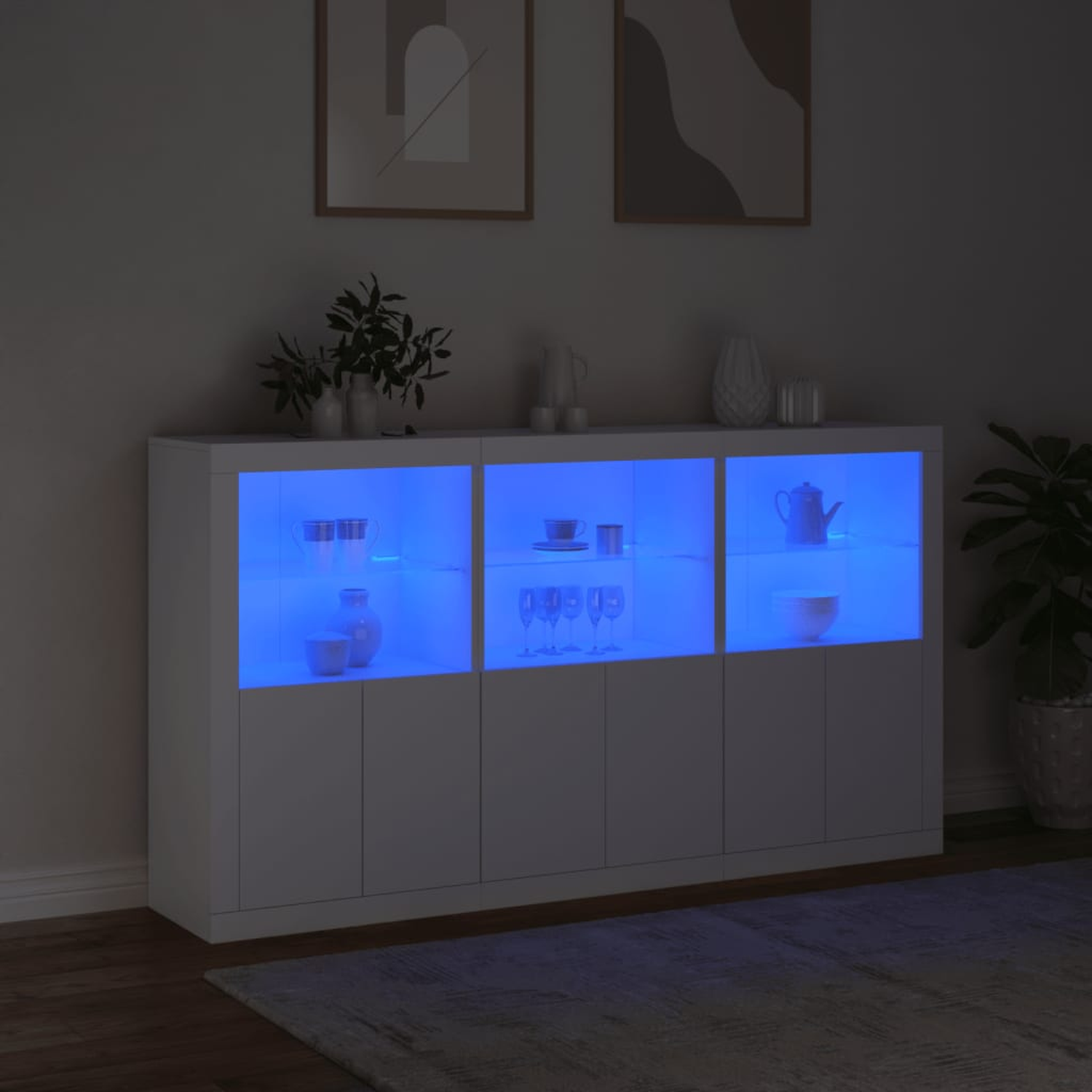 Weißer Schrank mit blauen Innenlichtern, der Gegenstände zeigt. Dunkler Raum, zwei gerahmte Bilder.