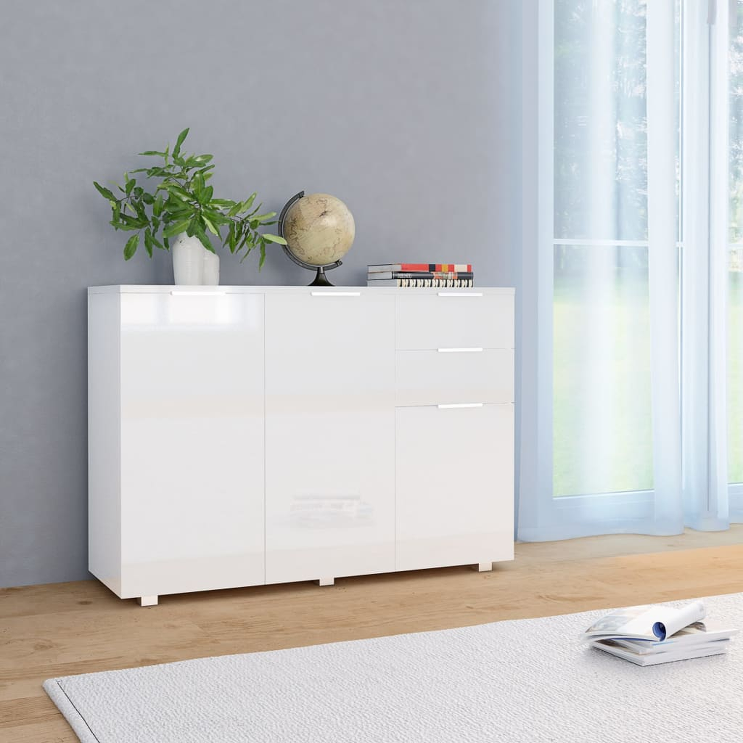 Weißer Schrank mit drei Türen und zwei Schubladen vor grauer Wand. Pflanze, Globus und Bücher oben drauf.